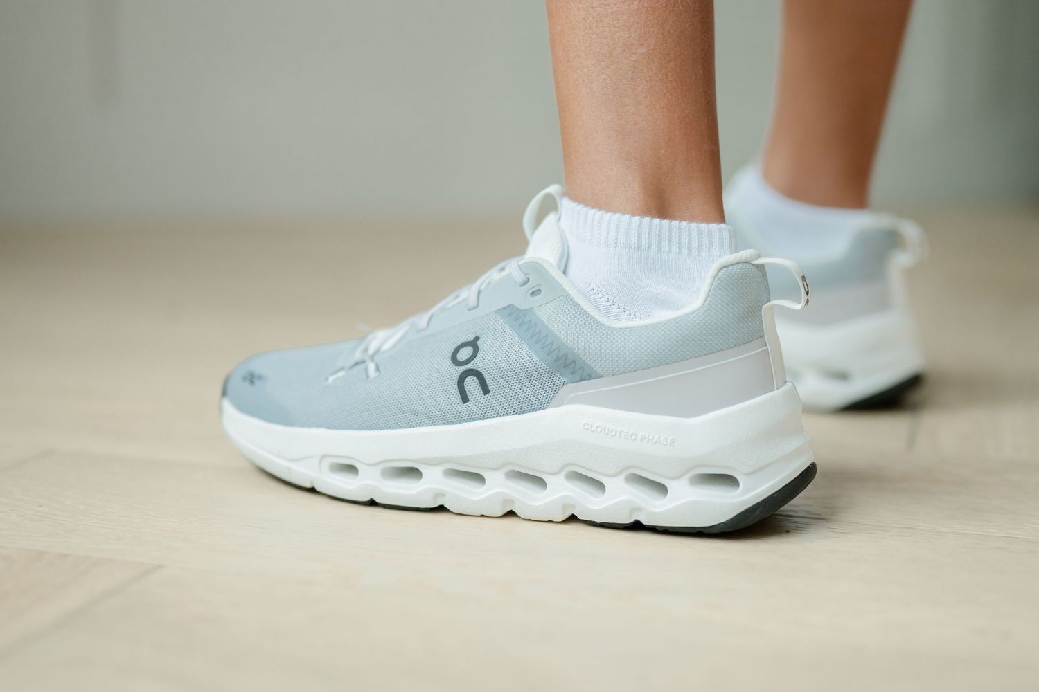 Closeup of white On Cloud running shoes worn with low white socks, seen from a floor view to the left, showing the sides.