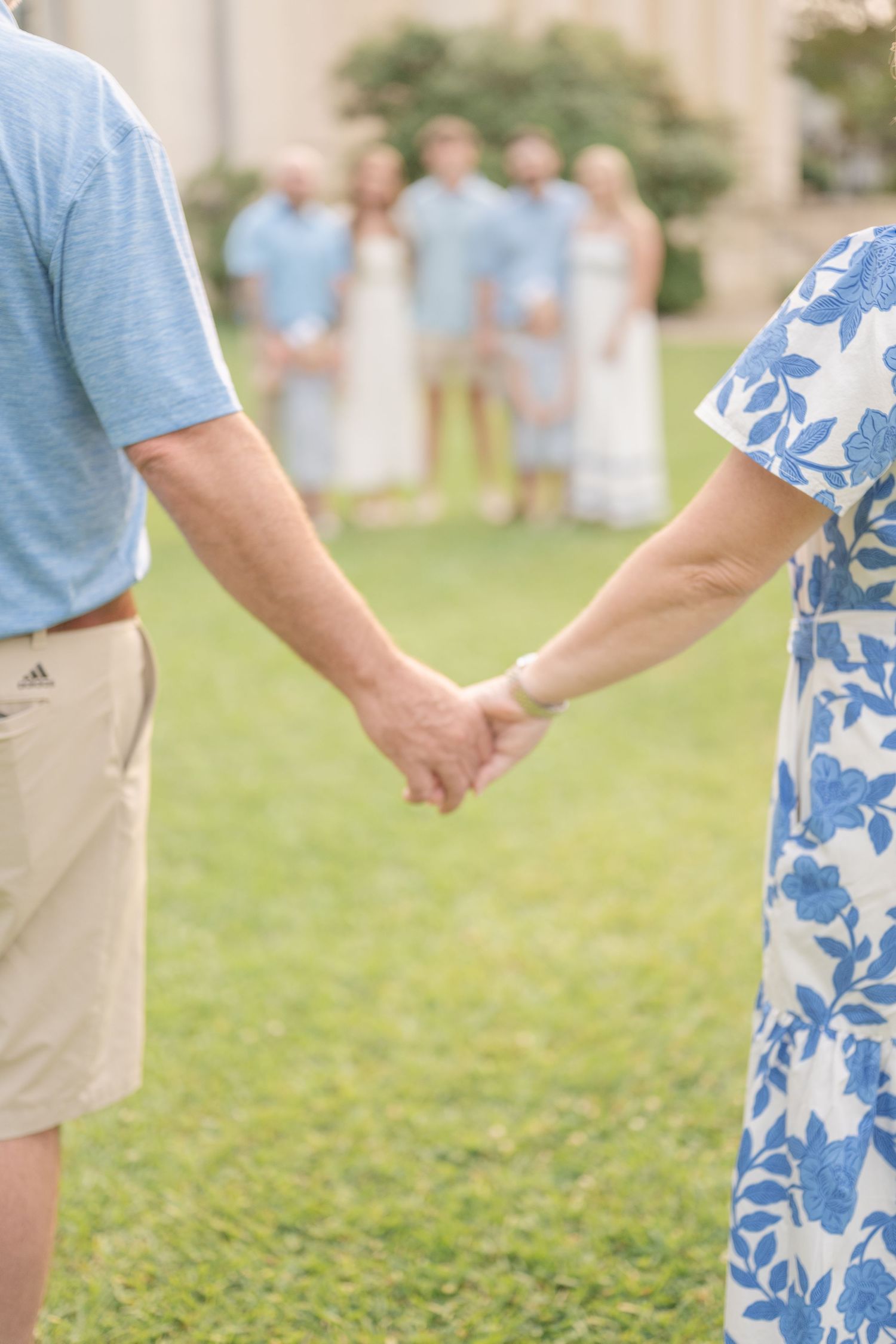 A couple holds hands while wearing coordinating blue and floral outfits on a grassy lawn.