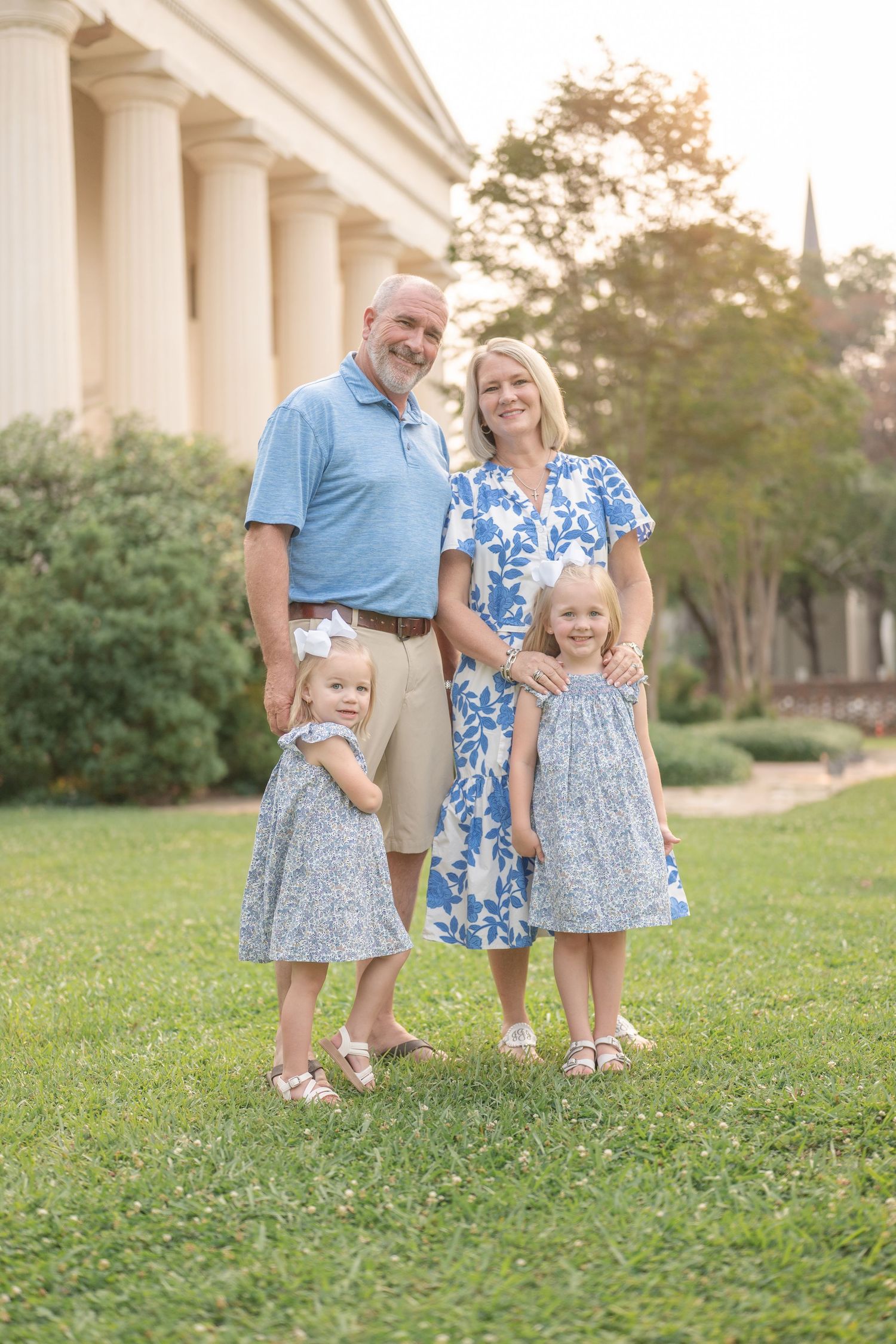 A family of four poses together in coordinating blue and gray outfits in front of a columned building.