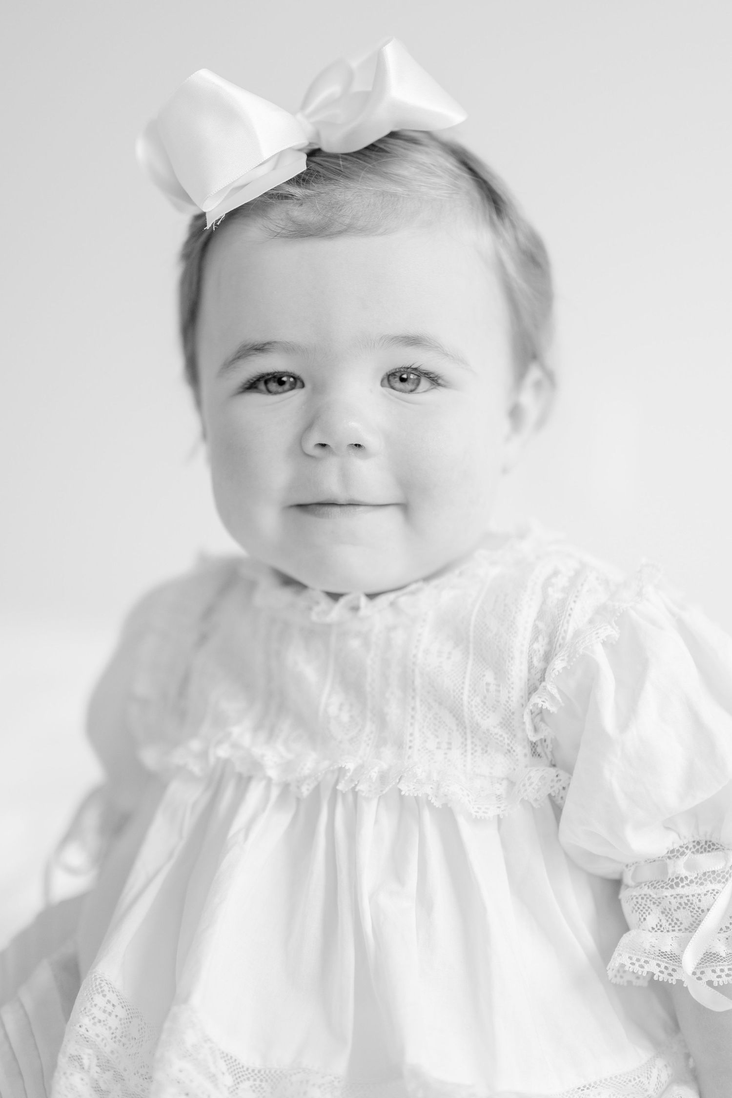 Baby wearing vintage white lace dress and bow in classic black and white portrait series.