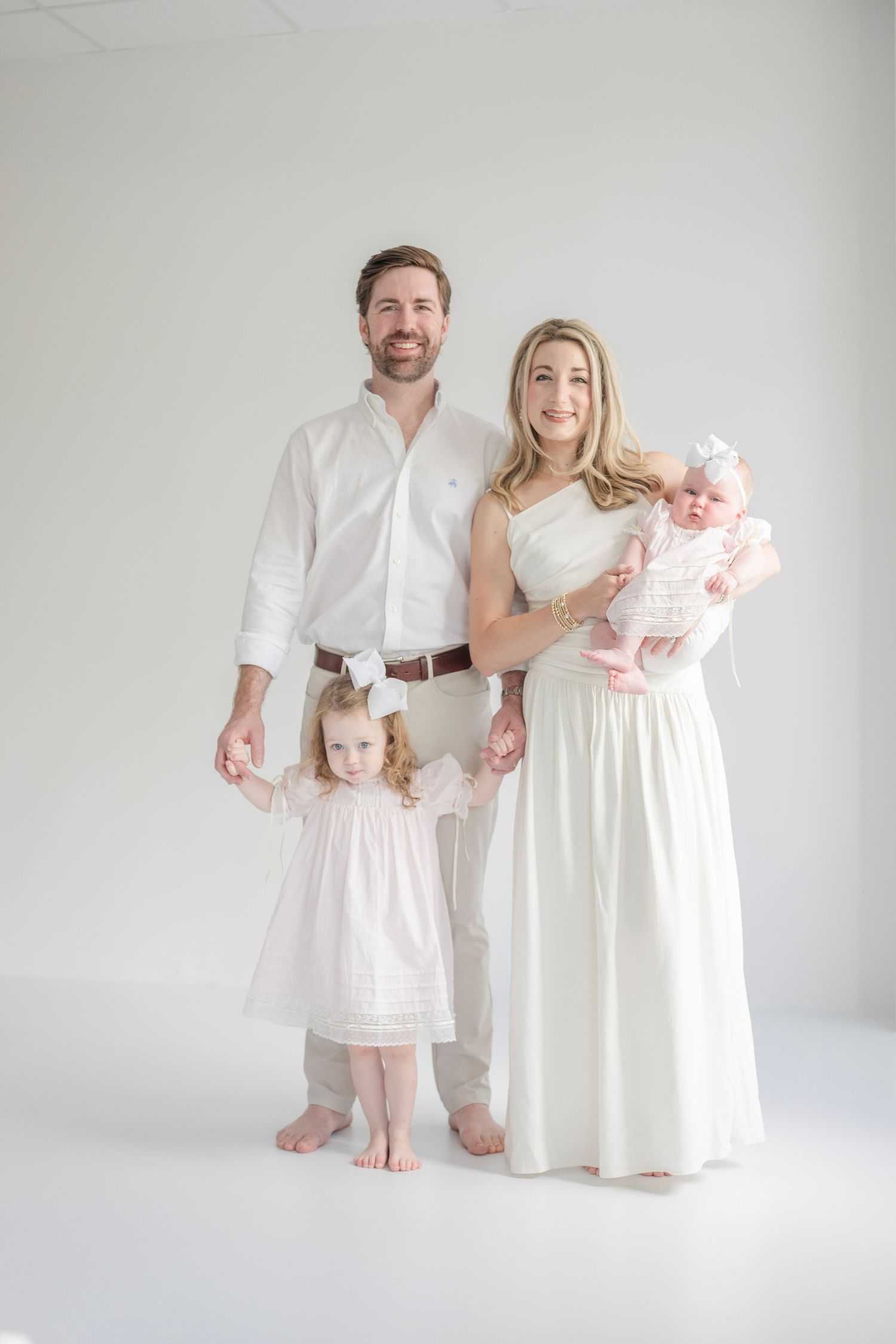 A family poses together in all white outfits against a minimalist white background.