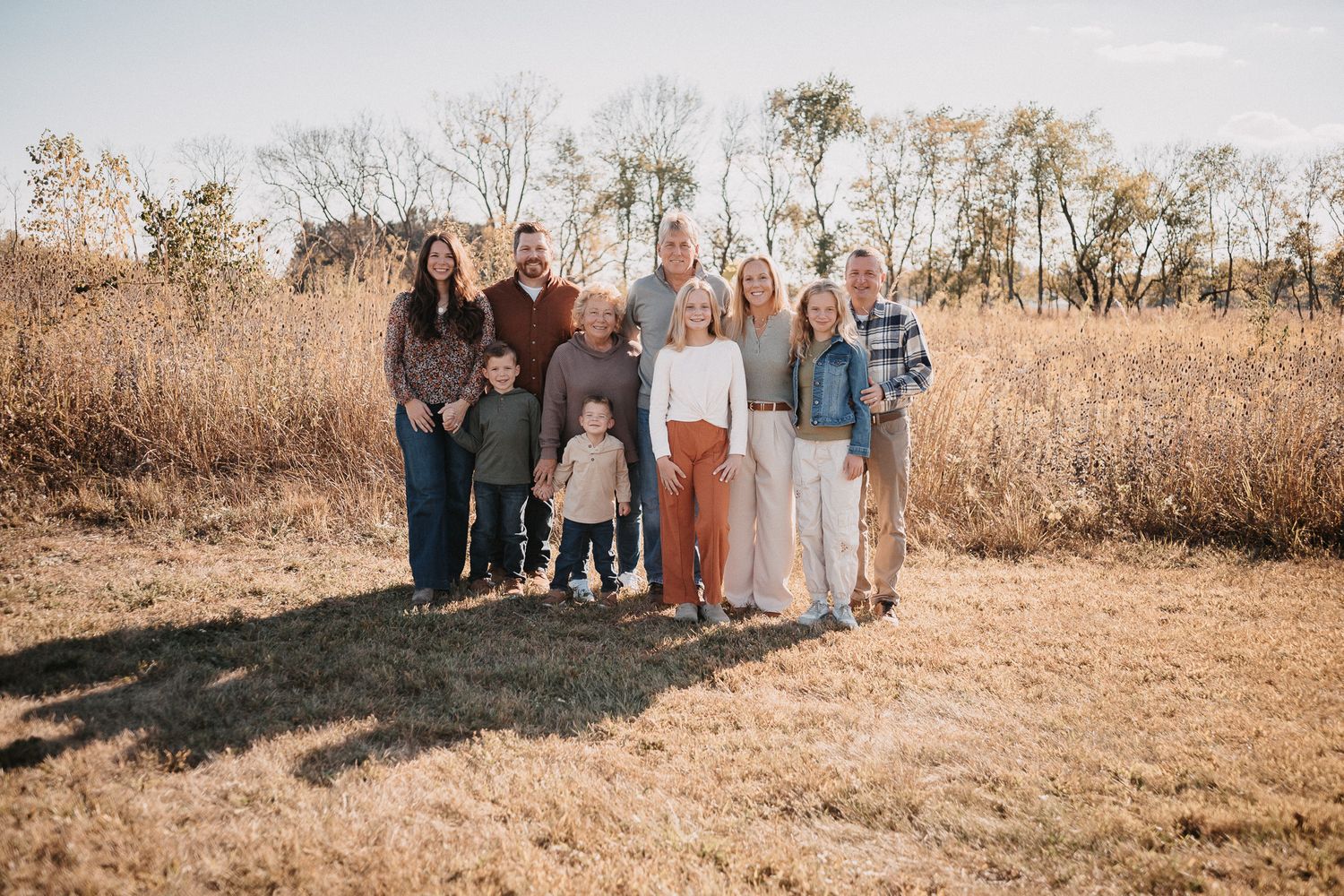 A group of people stand together in an autumn field with golden grass and trees during sunset.