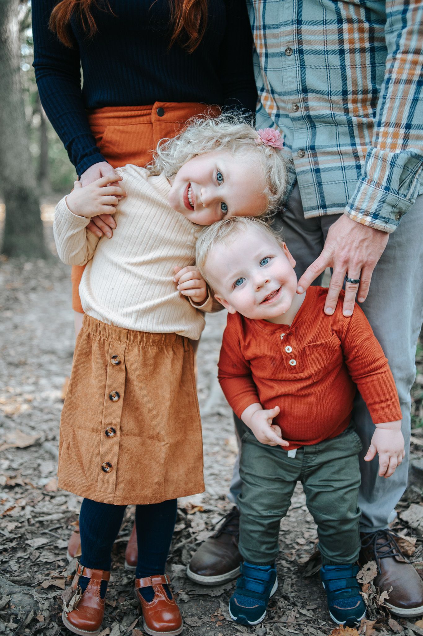Two children in stylish fall outfits stand together outdoors wearing earth-toned clothing and smiling.