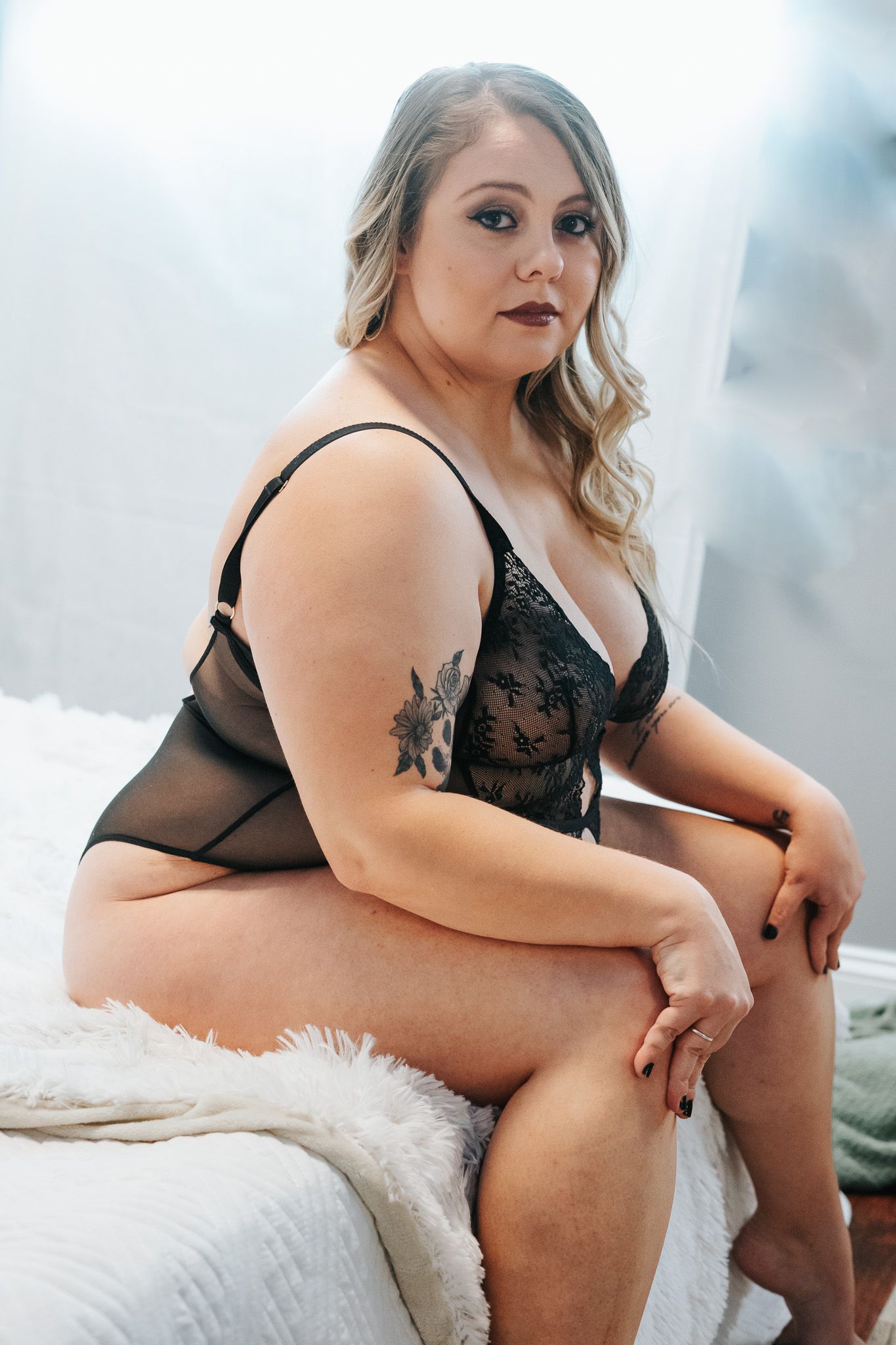 Intimate boudoir photo series showing a person in black lingerie posing on white fur bedding.