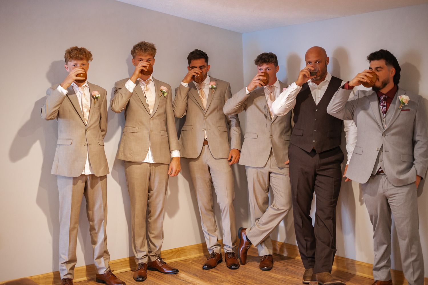 Groomsmen strike playful poses wearing coordinated beige and gray suits during a wedding photo session.