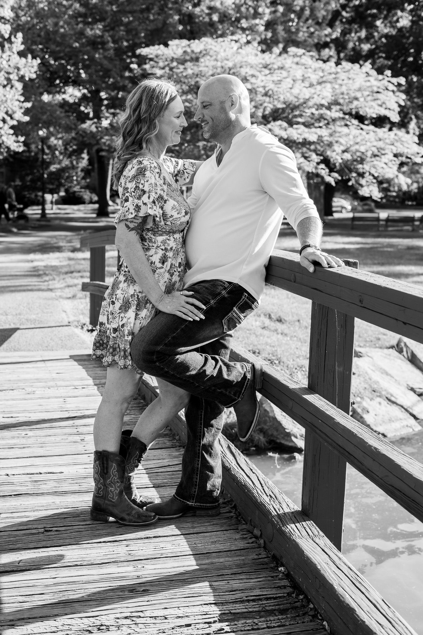 A romantic couple shares an intimate moment on a wooden bridge in a park setting, captured in black and white.