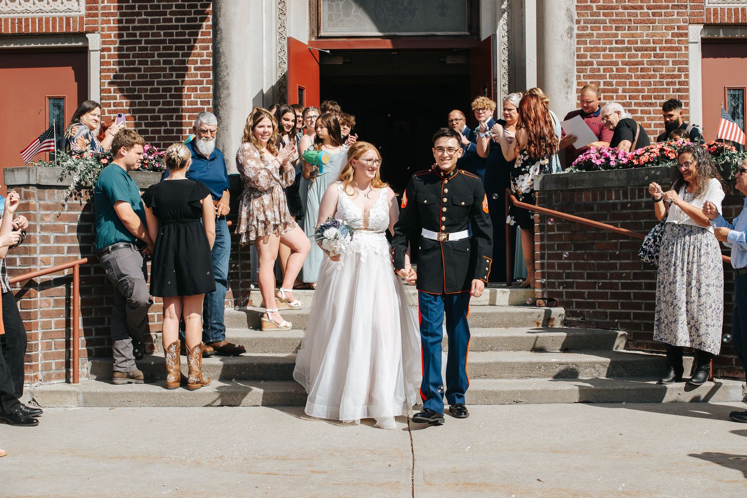 Wedding ceremony guests gather outside a brick church building on a sunny day.
