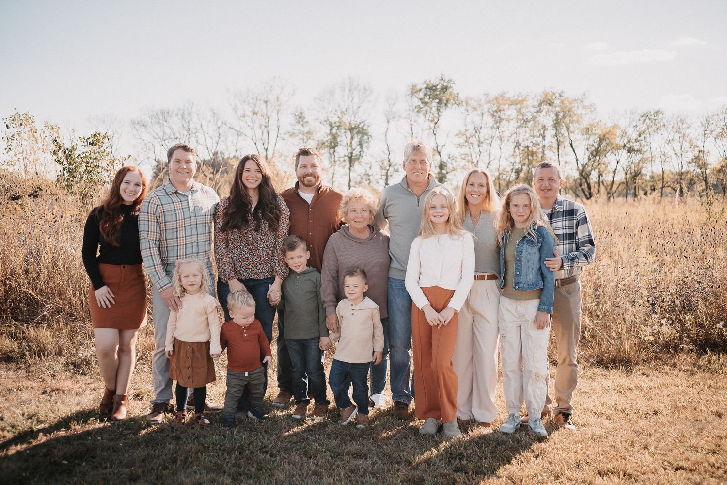 A group of people standing together in a golden field during sunset wearing coordinated neutral-toned outfits.