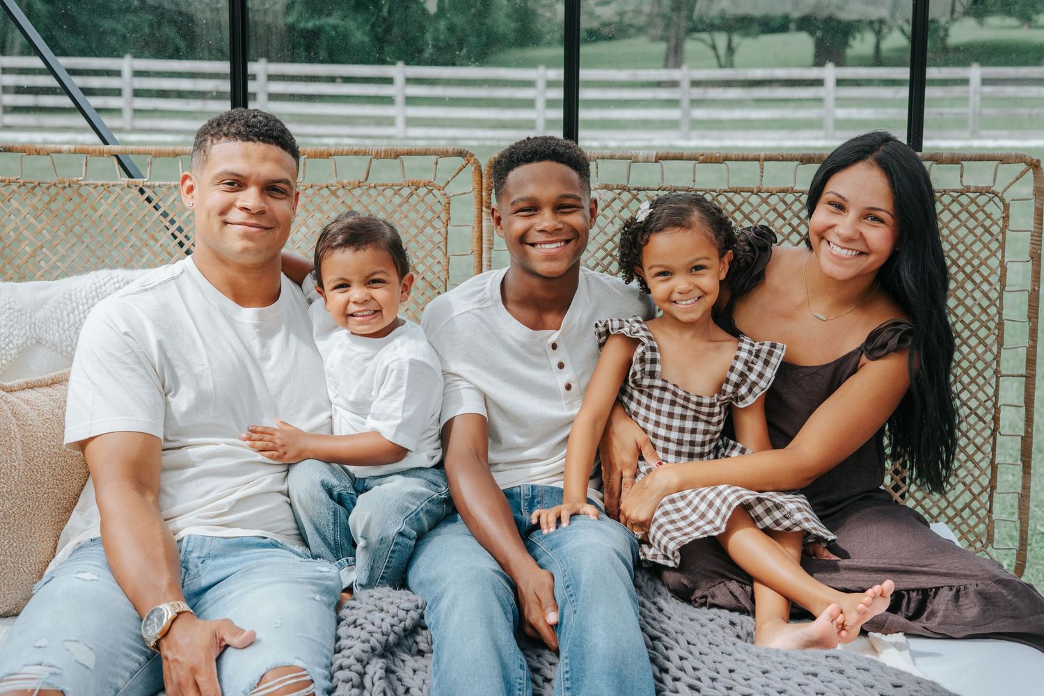Happy family of five smiling together on a cozy outdoor patio sofa, featuring two adults and three young children.