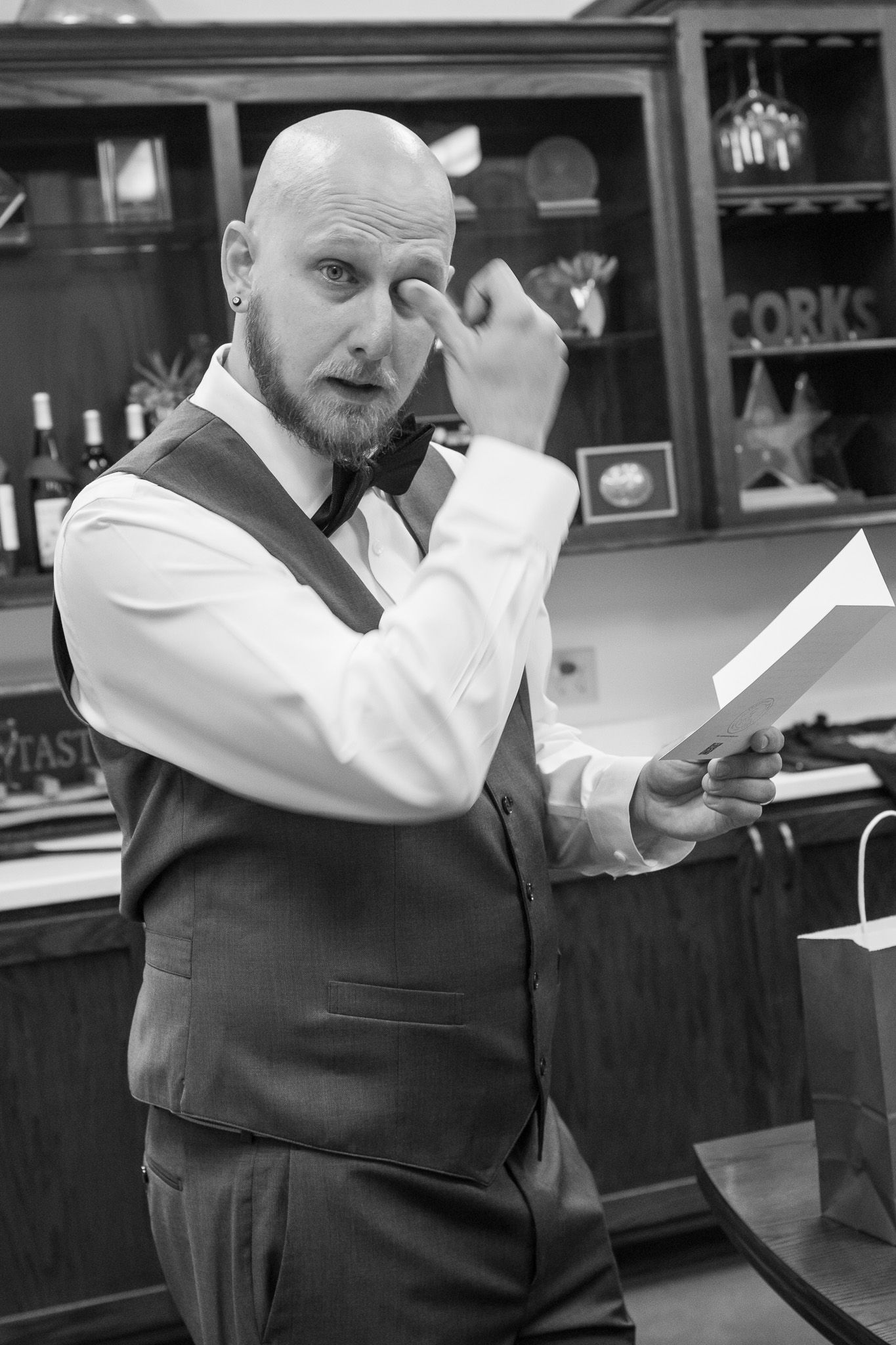 A person in a black vest and white shirt reading a document while making expressive gestures in a restaurant setting.