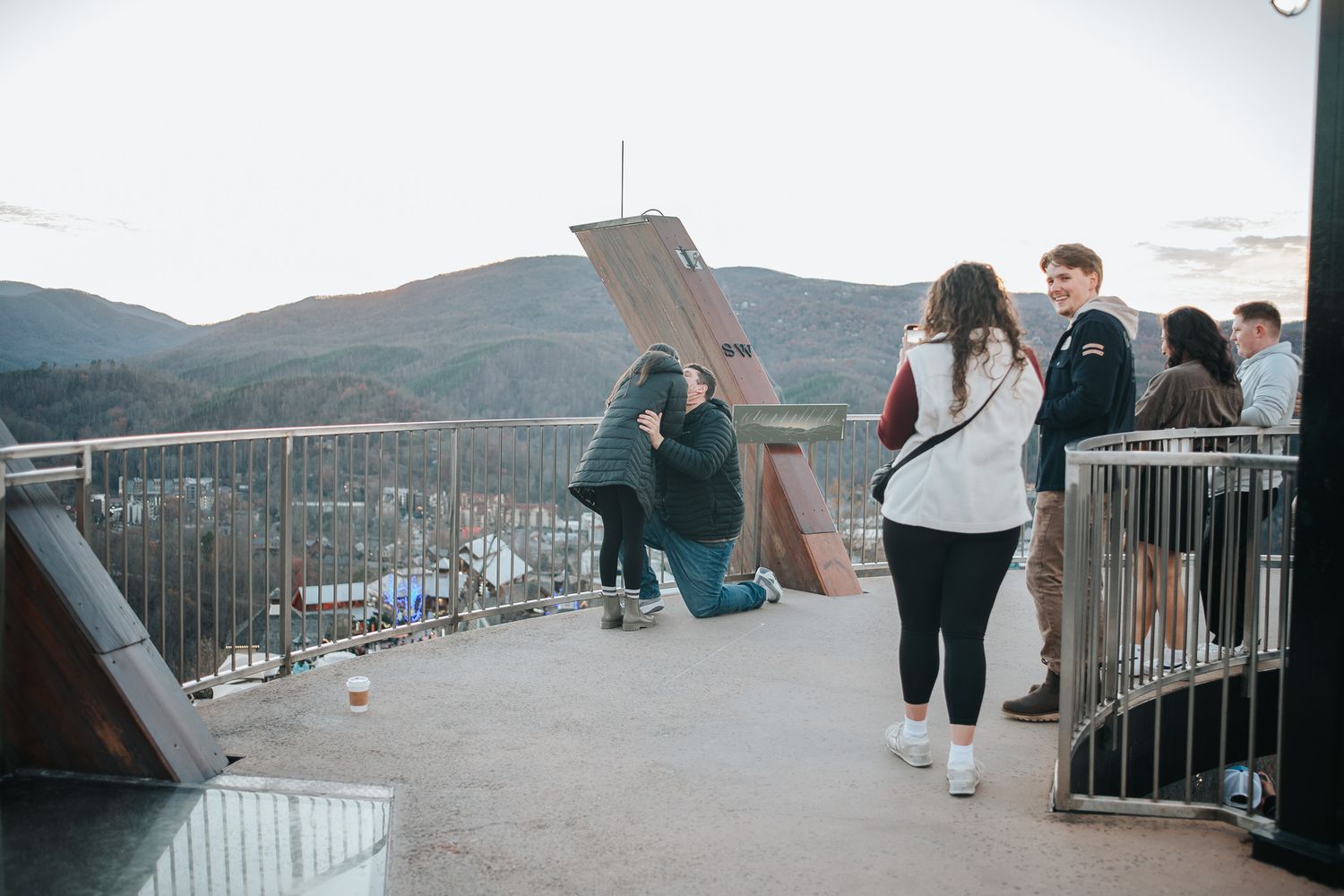 People enjoying scenic mountain views from a modern observation deck with glass railings and benches.