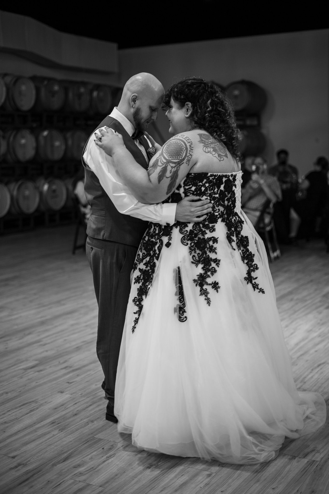 Black and white wedding photos of couple dancing together at a reception venue with wine barrels in the background.