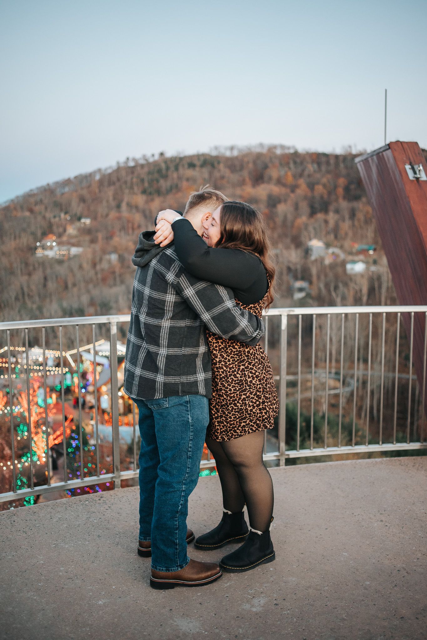 A couple embracing on an observation deck overlooking a scenic mountain landscape.