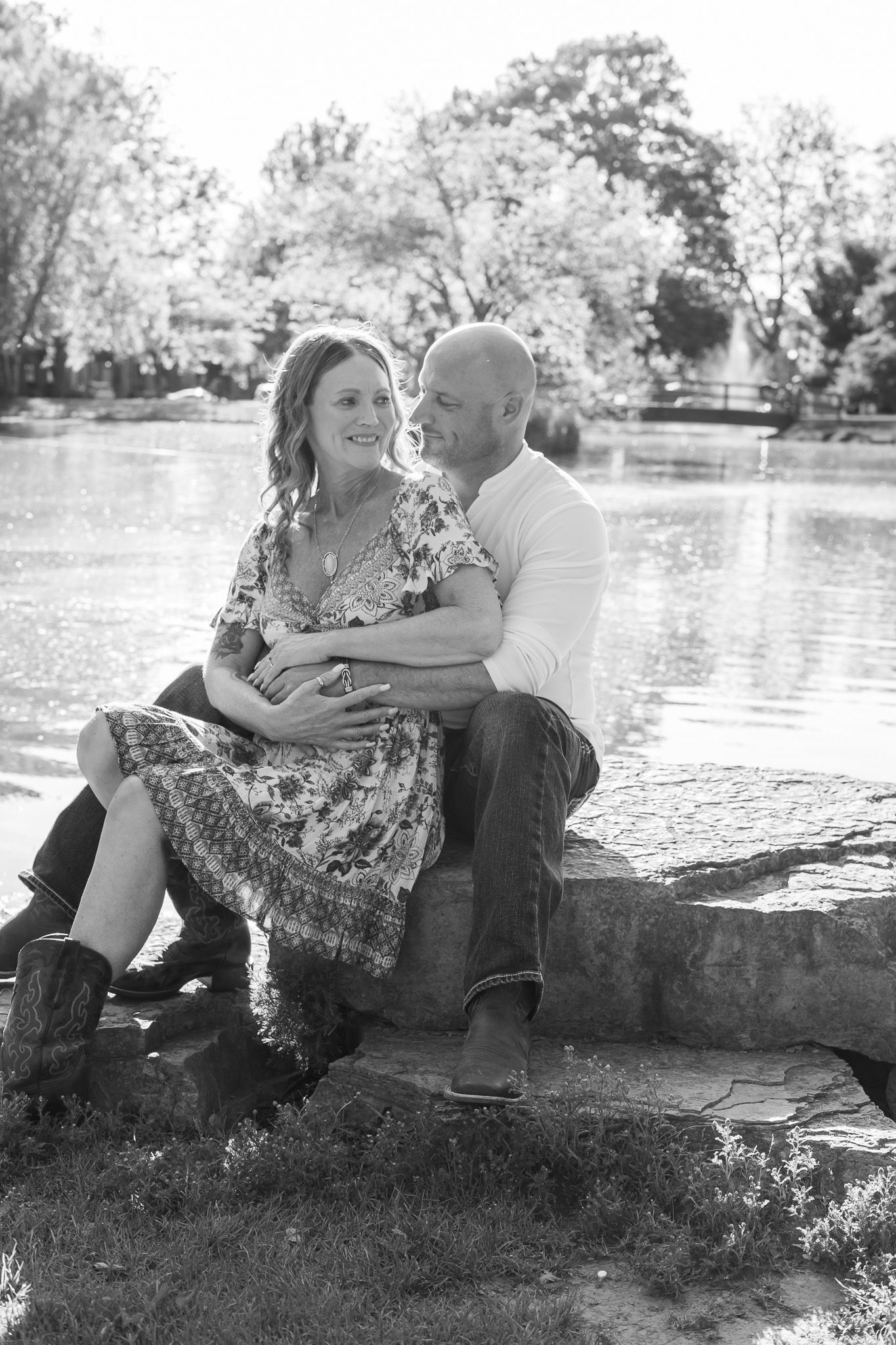 Black and white romantic portrait of couple sitting together by a lake in a natural outdoor setting.