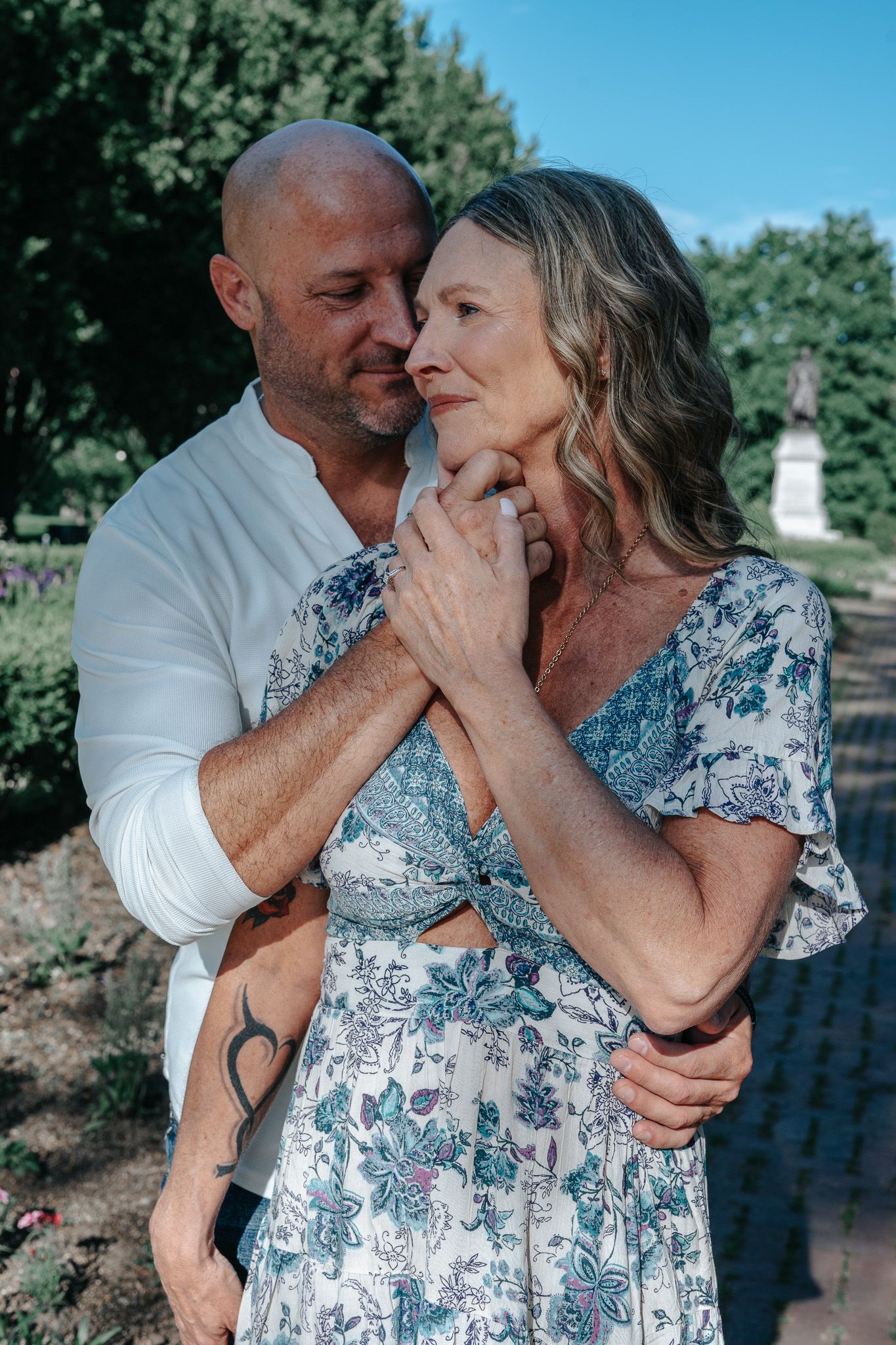 A tender outdoor portrait of a couple in an emotional embrace, with her wearing a floral dress and him in white.