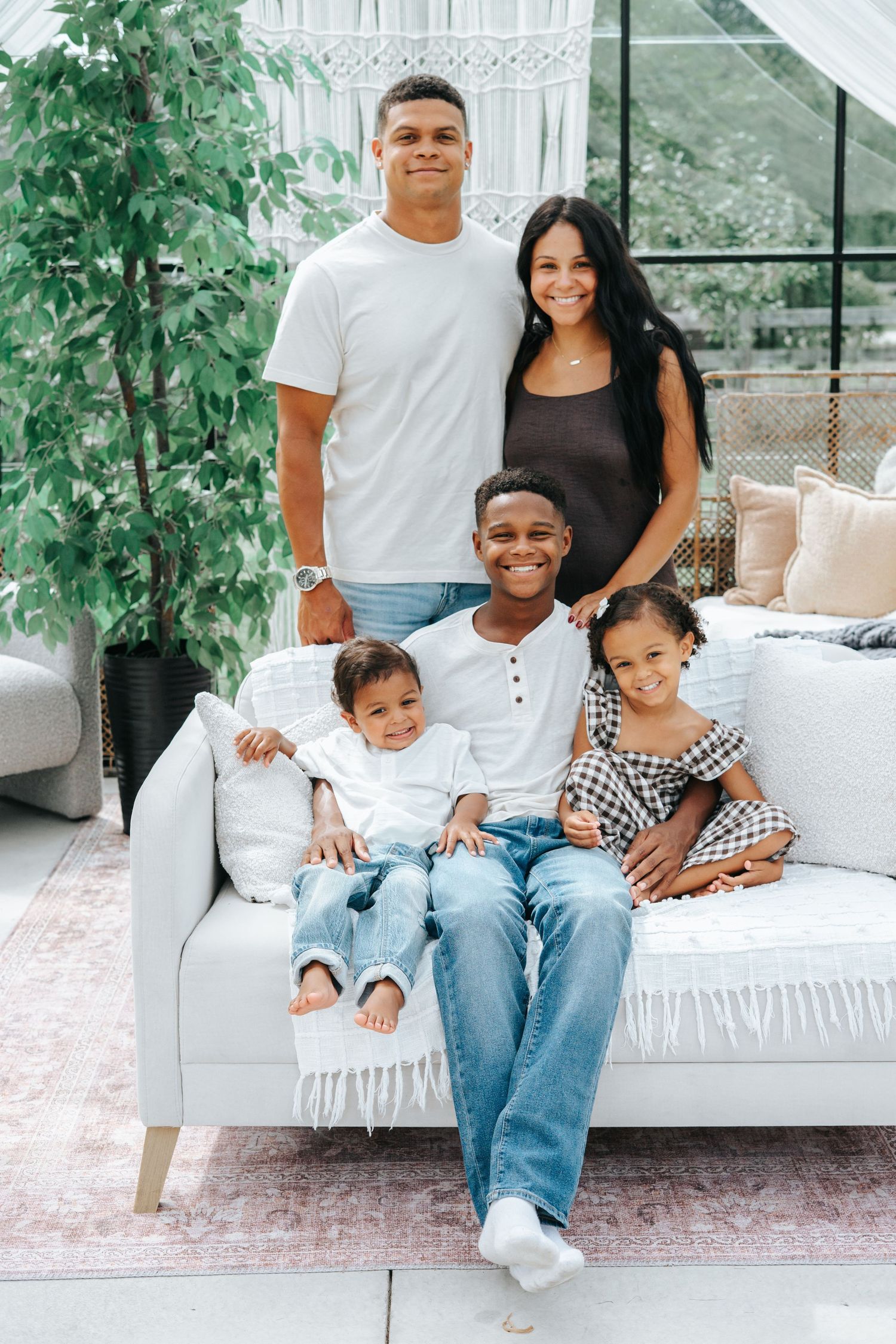 A happy family of five poses together in a modern living room, with two parents standing behind three children on a couch.