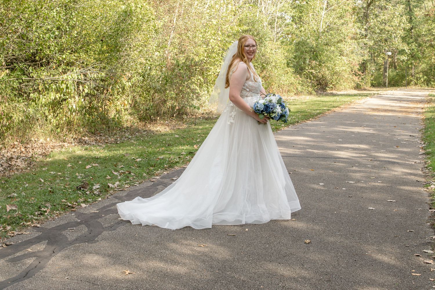 Wedding couple walks along a tree-lined path during an outdoor photo session.