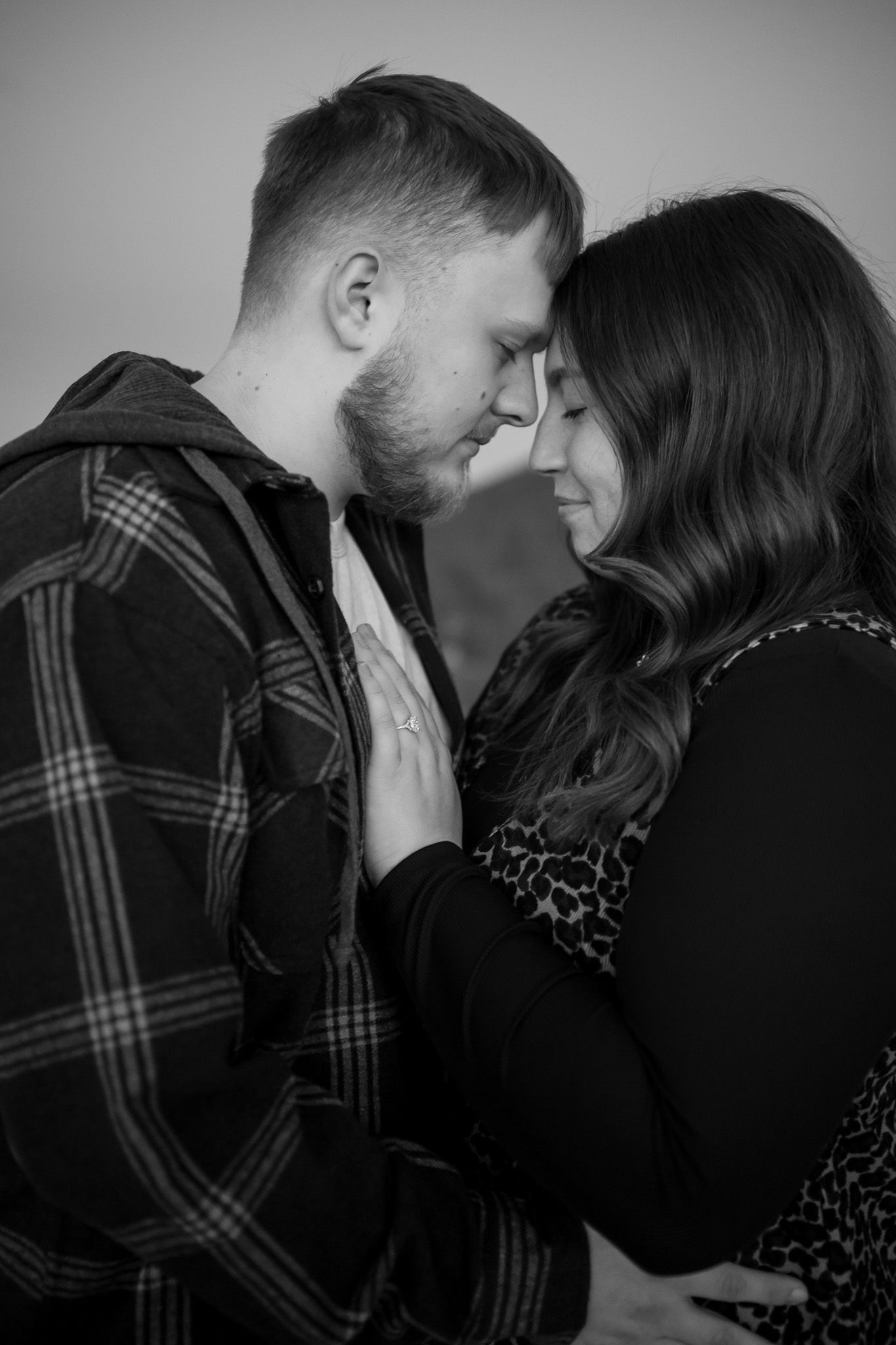 Black and white photo of a romantic couple sharing an intimate moment, foreheads touching tenderly.
