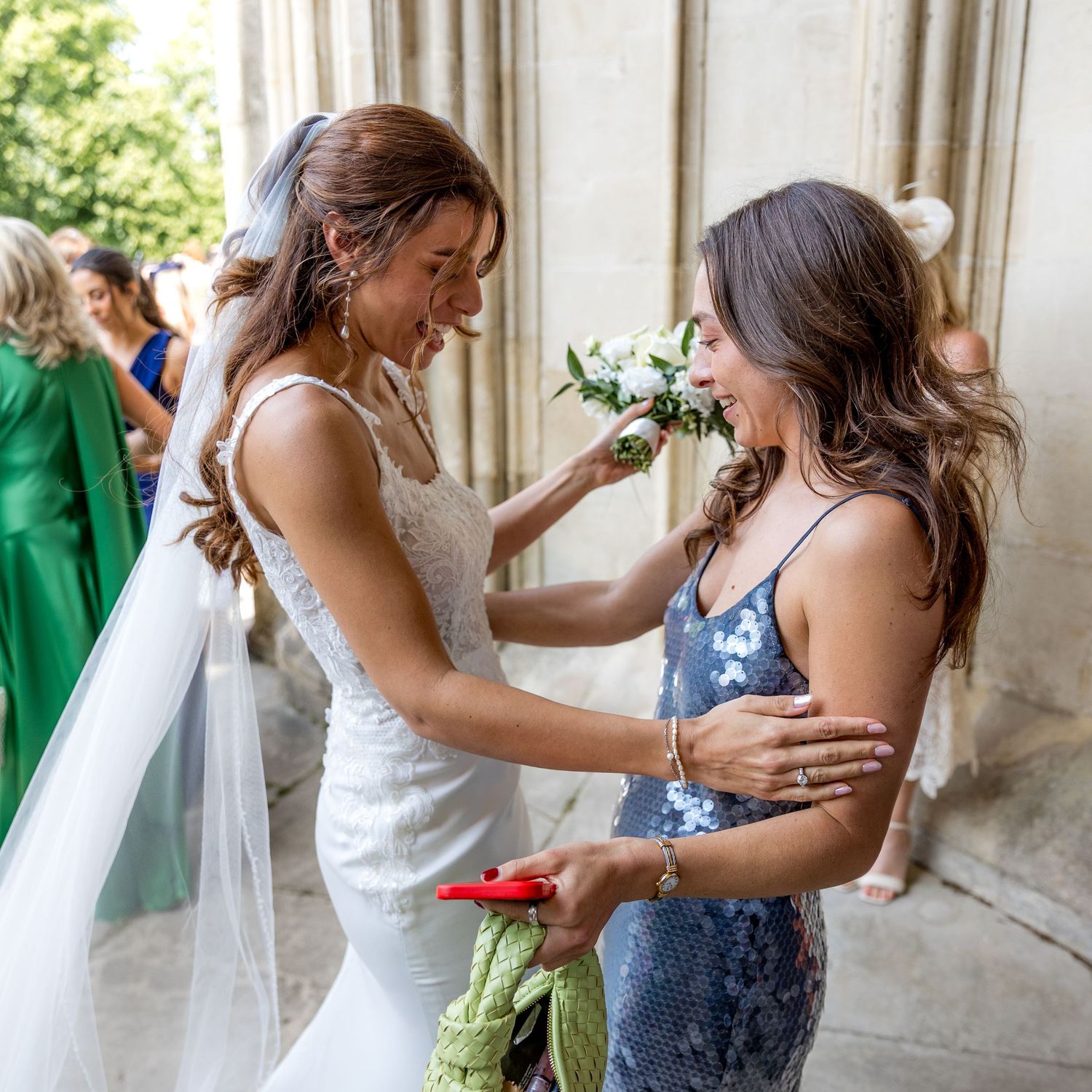 Wedding party sharing joyful moments and embraces in an elegant stone corridor.