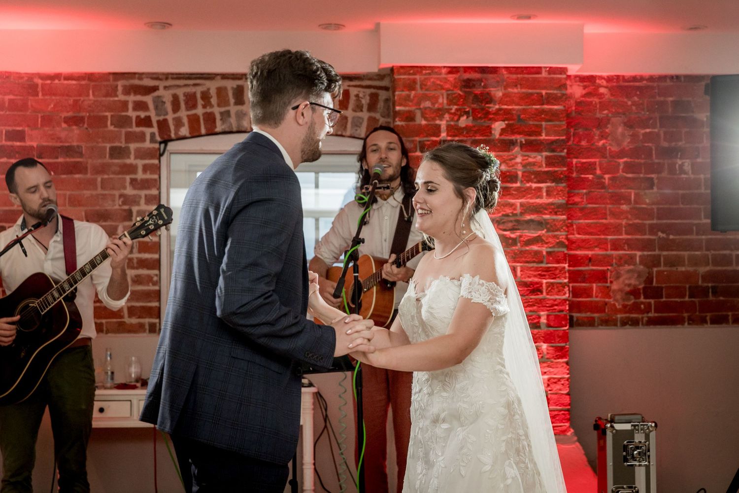 Wedding reception guests dancing and celebrating on a dance floor with red ambient lighting and brick walls.