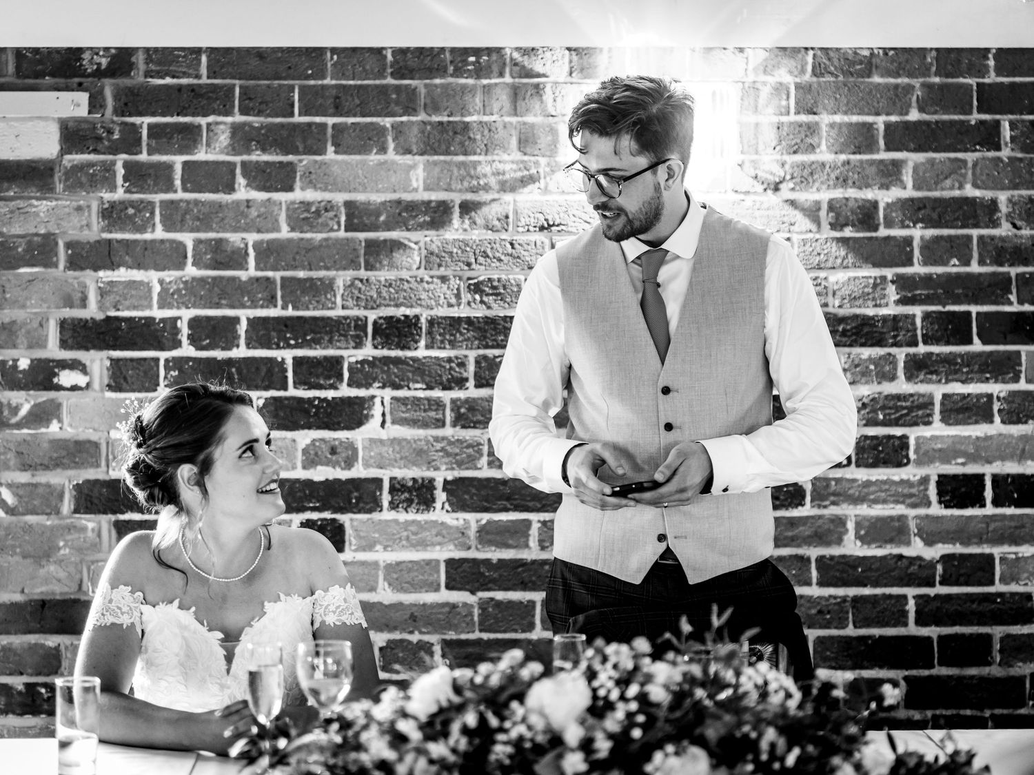 Wedding guests enjoying a meal and conversation at a rustic brick-walled reception venue.
