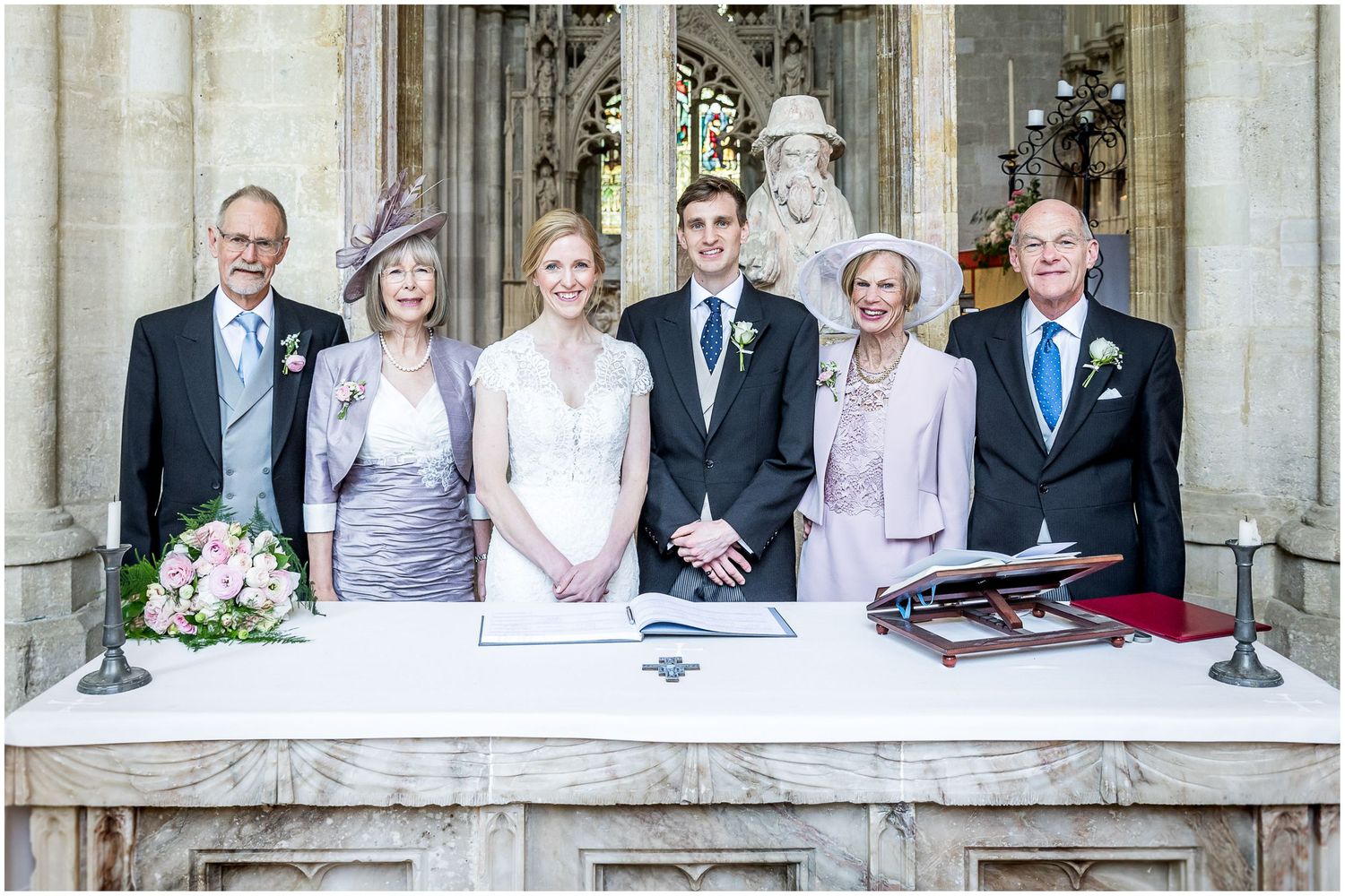 Wedding party poses together in formal attire at a historic stone church entrance.