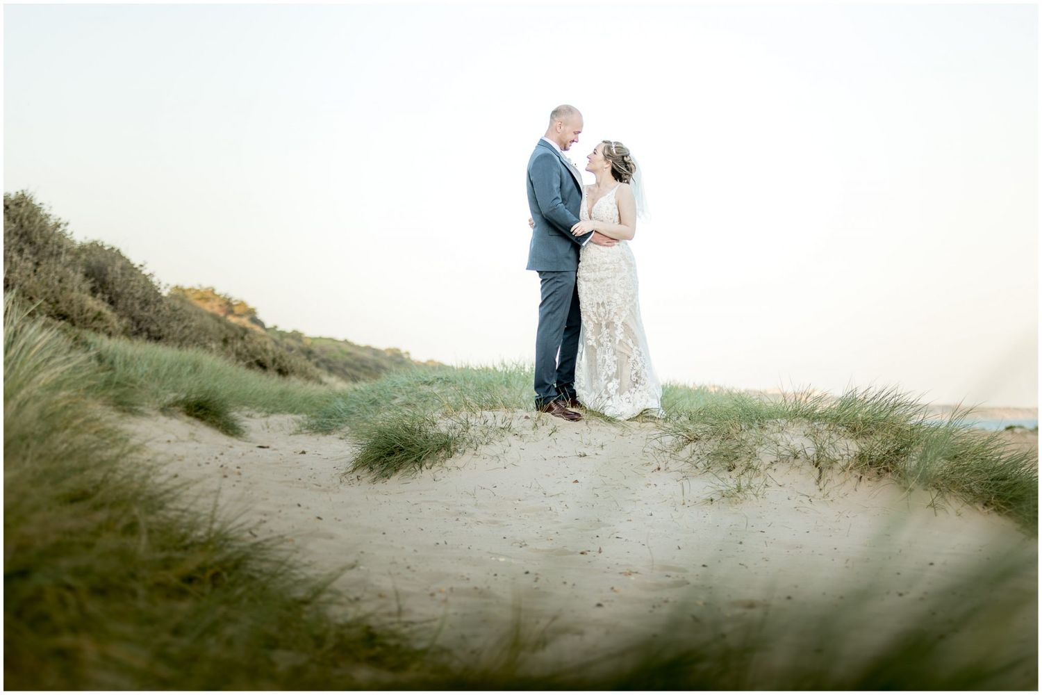Seaside wedding portraits on sandy dunes during golden hour.