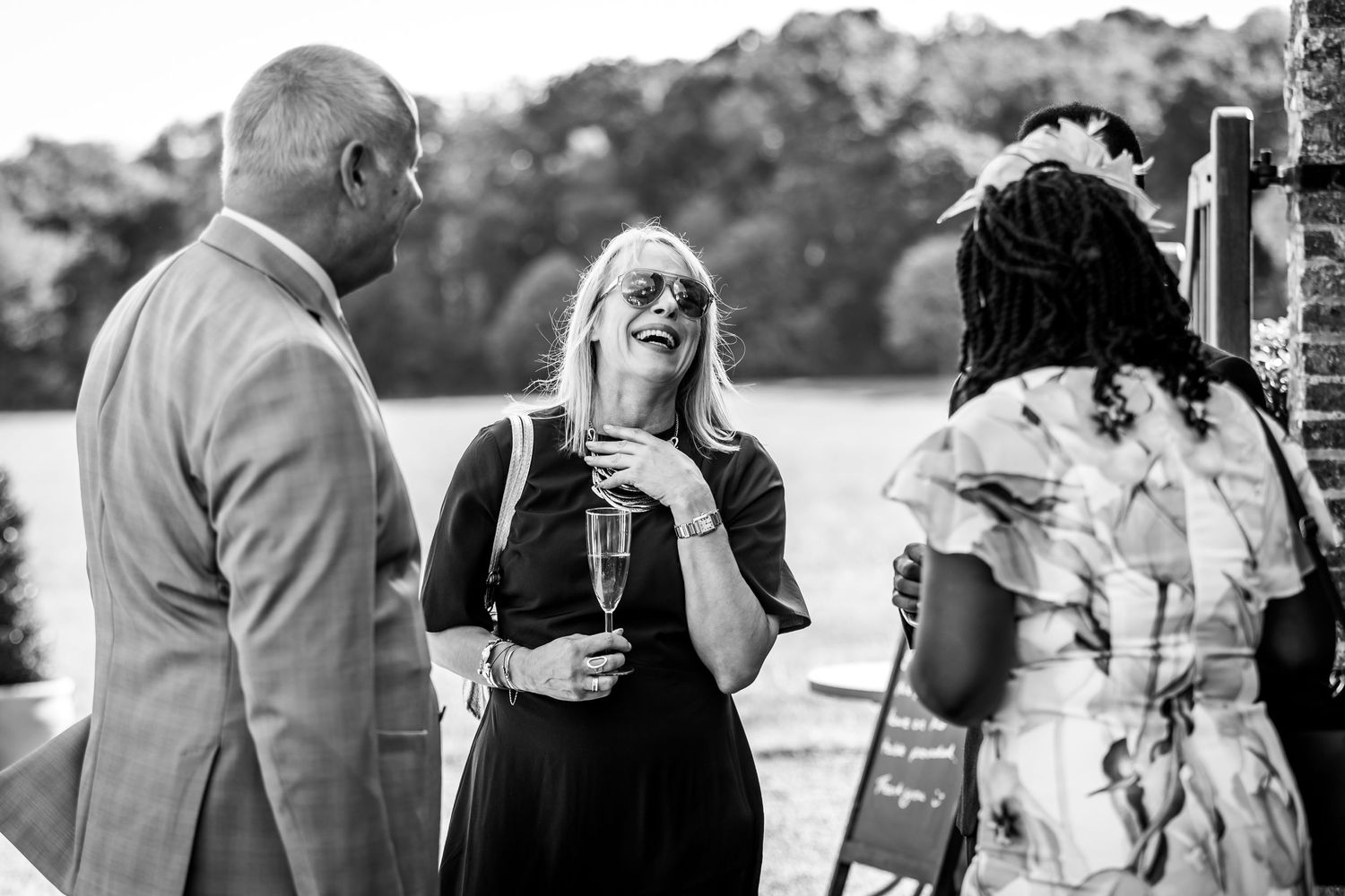 Wedding party members socialize during an outdoor celebration near brick walls.