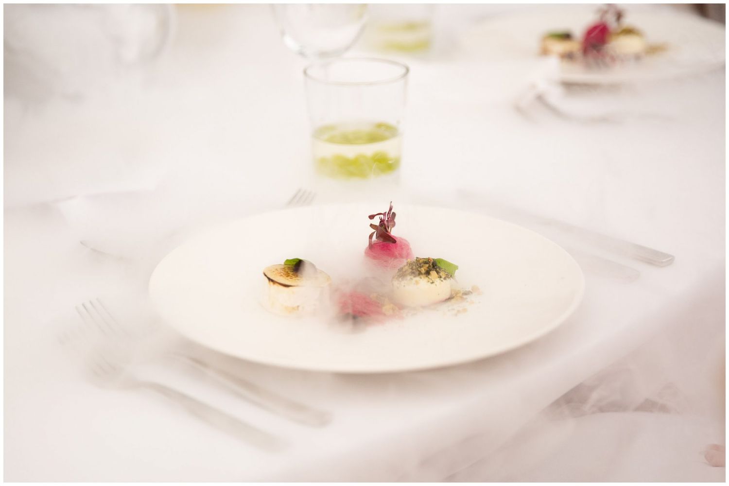 White plate with an elegant dessert garnished with delicate pink flowers and a light dusting of powdered sugar.