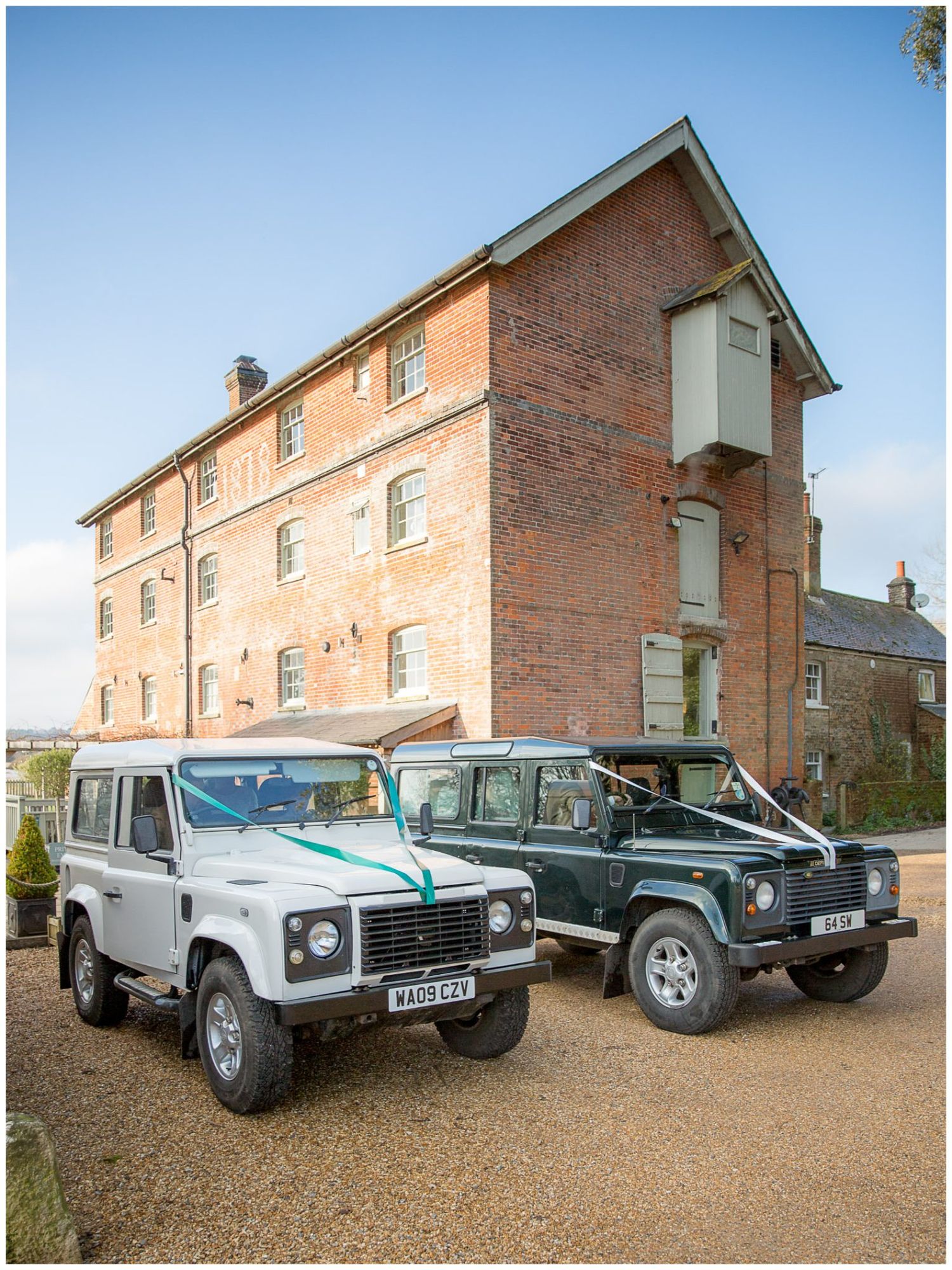 Collection of Land Rover vehicles parked outside brick building on gravel driveway.