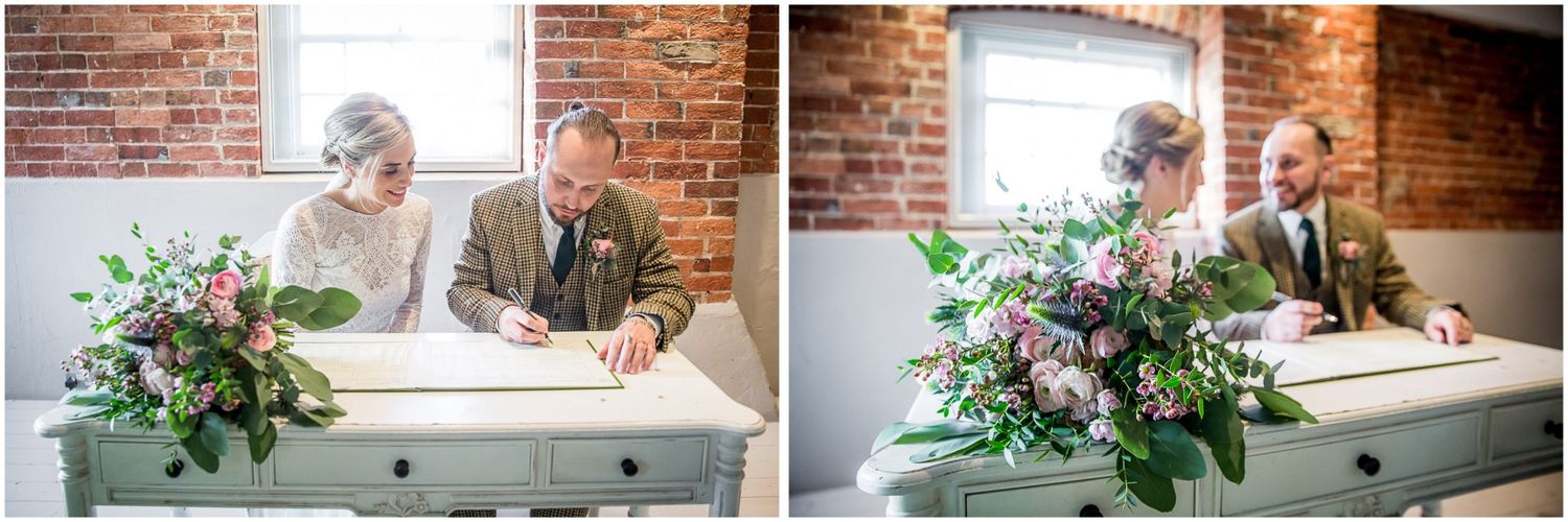 Couple signing documents at a white desk with floral arrangement during wedding ceremony.