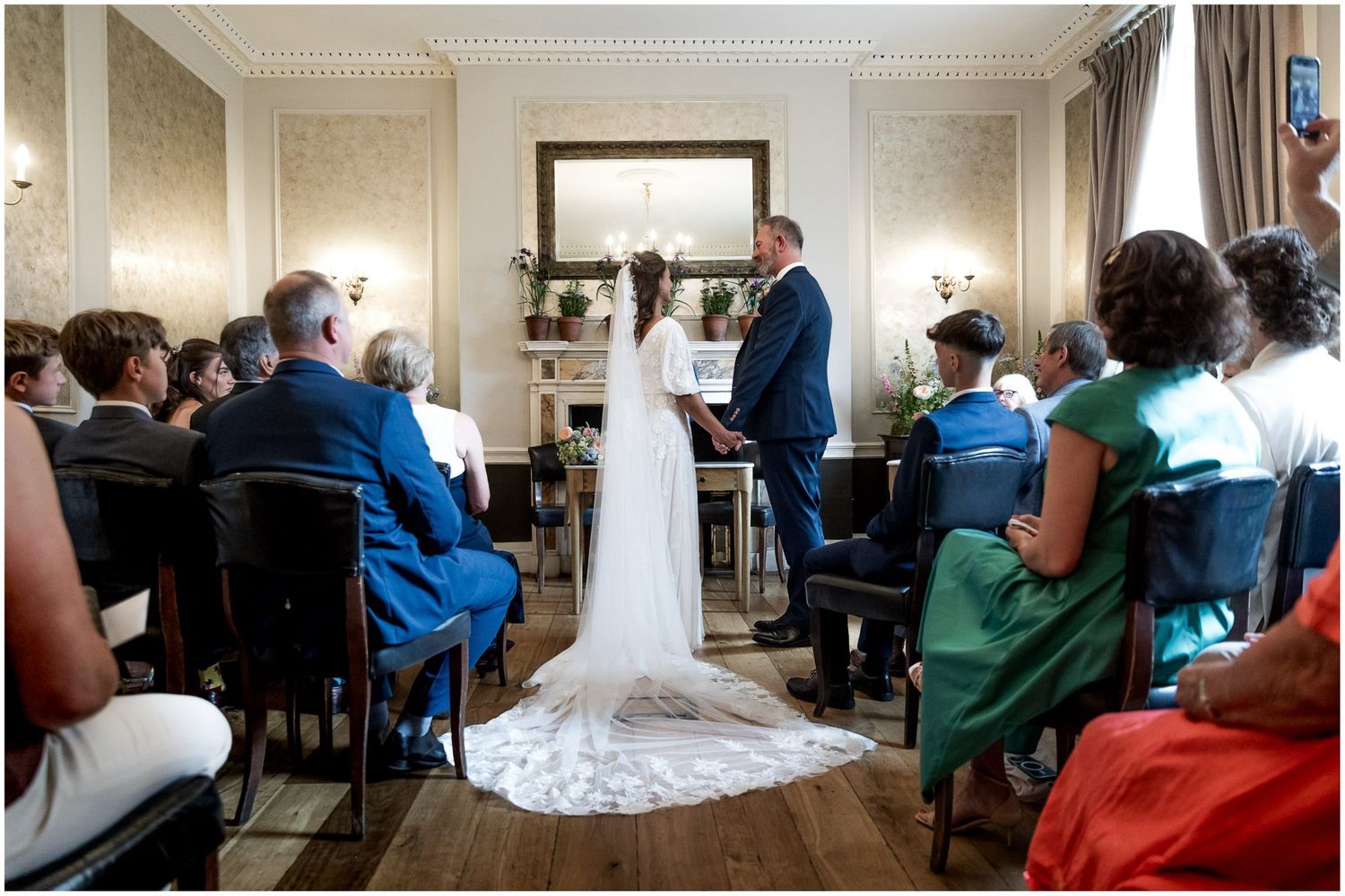 Wedding guests seated in rows during an indoor ceremony with elegant crown molding.