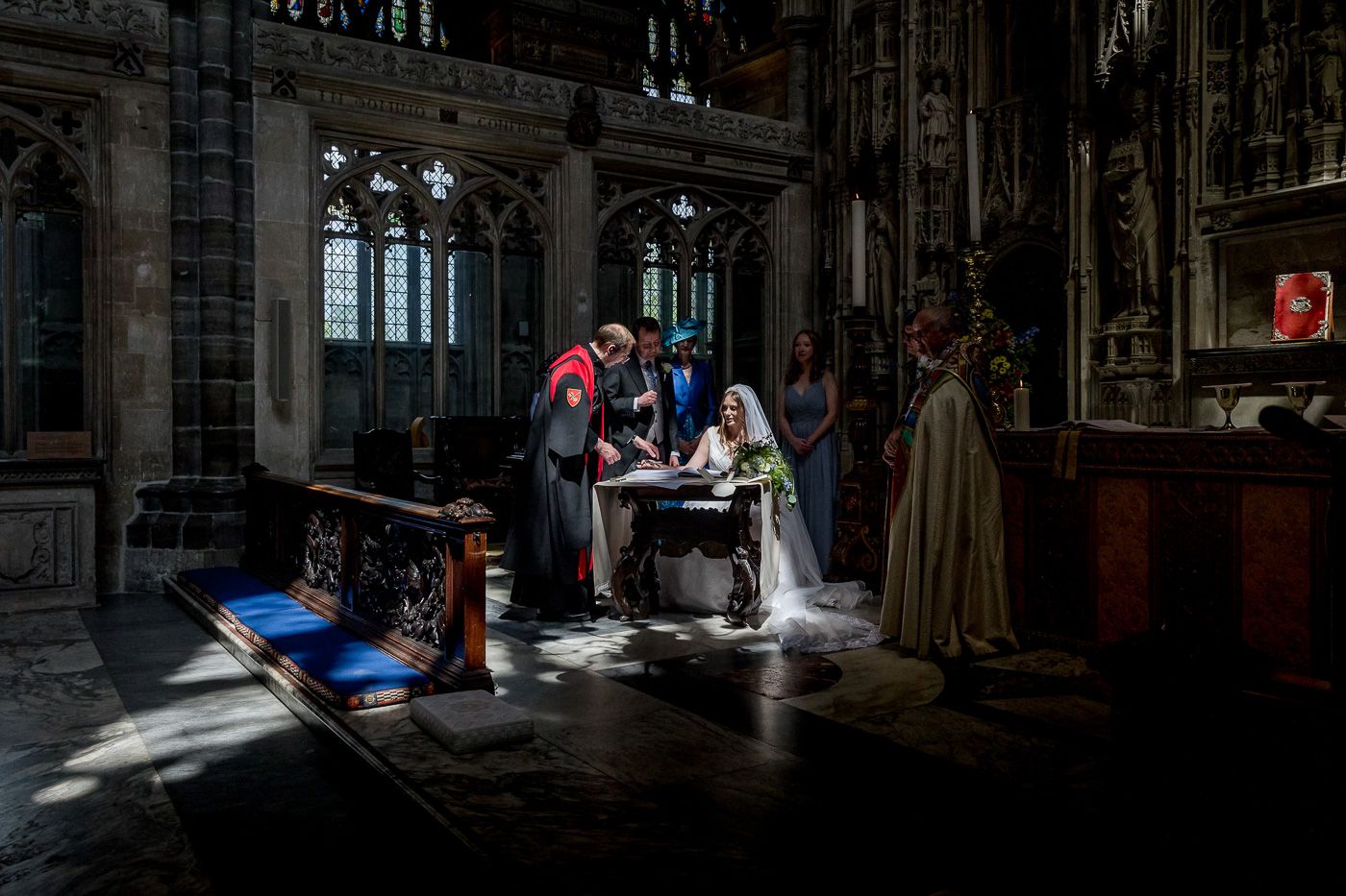 Dark cathedral interior with dramatic lighting streaming through stained glass windows.