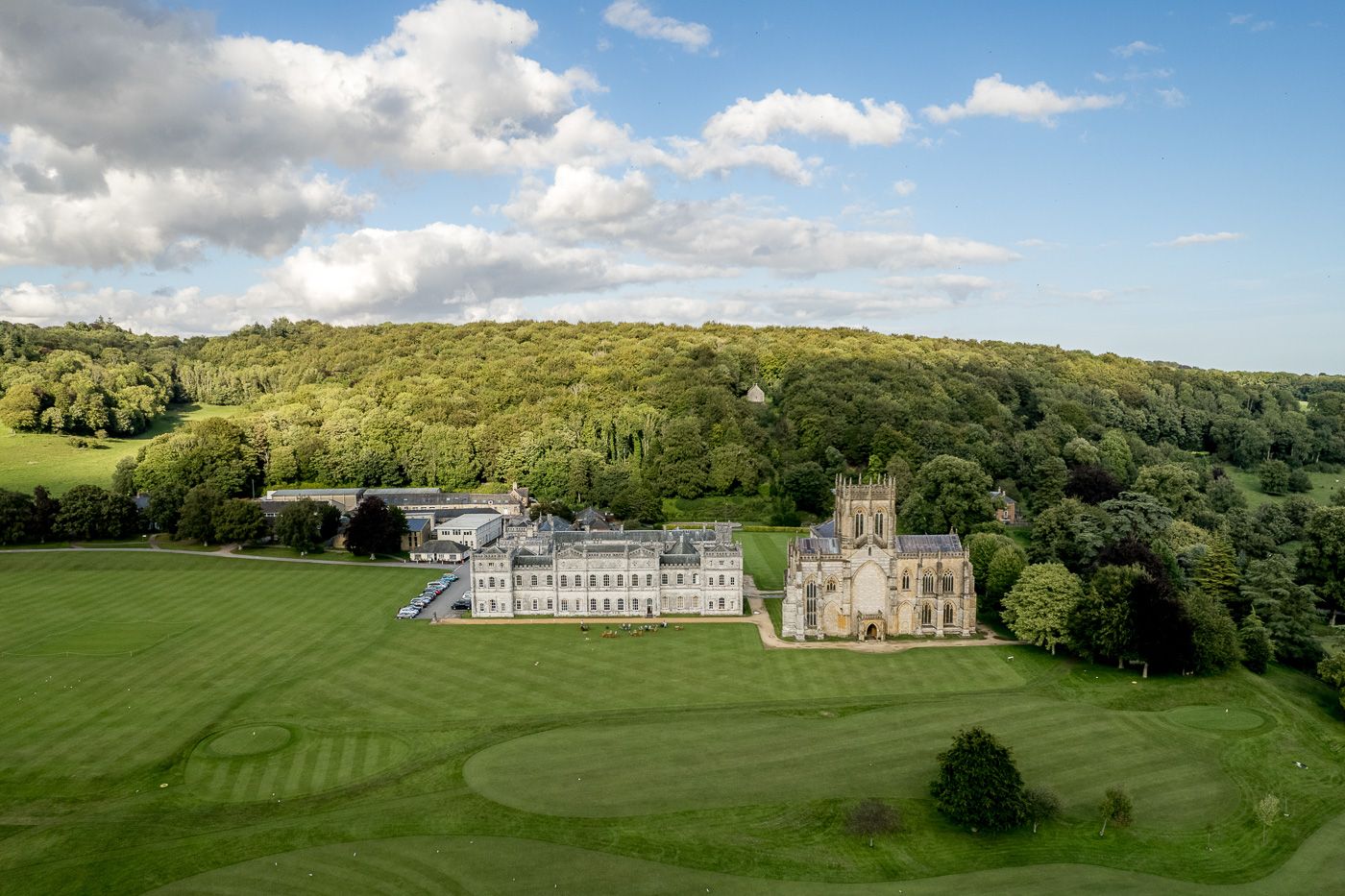 Aerial panorama of a grand estate with manicured lawns and historic buildings surrounded by lush forest.
