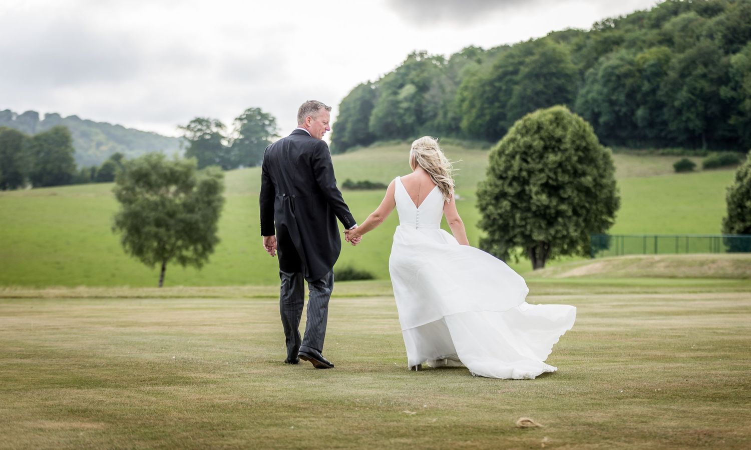 Wedding couple walking through rolling green countryside with dramatic cloudy skies.