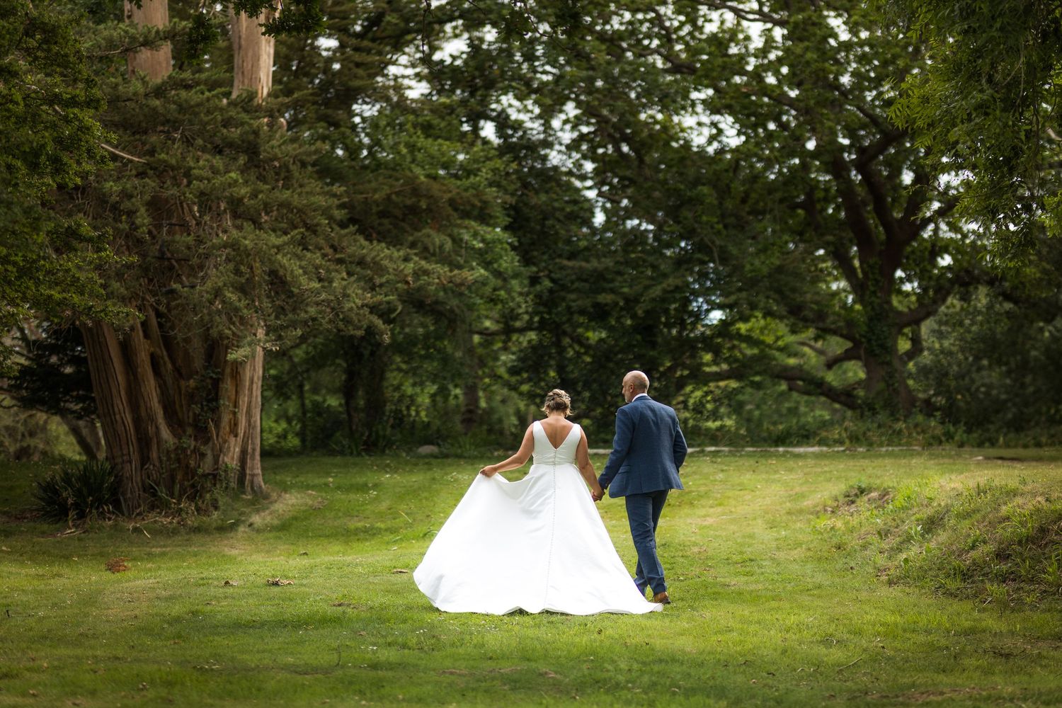 Couple poses for romantic wedding photos in a lush green garden setting.
