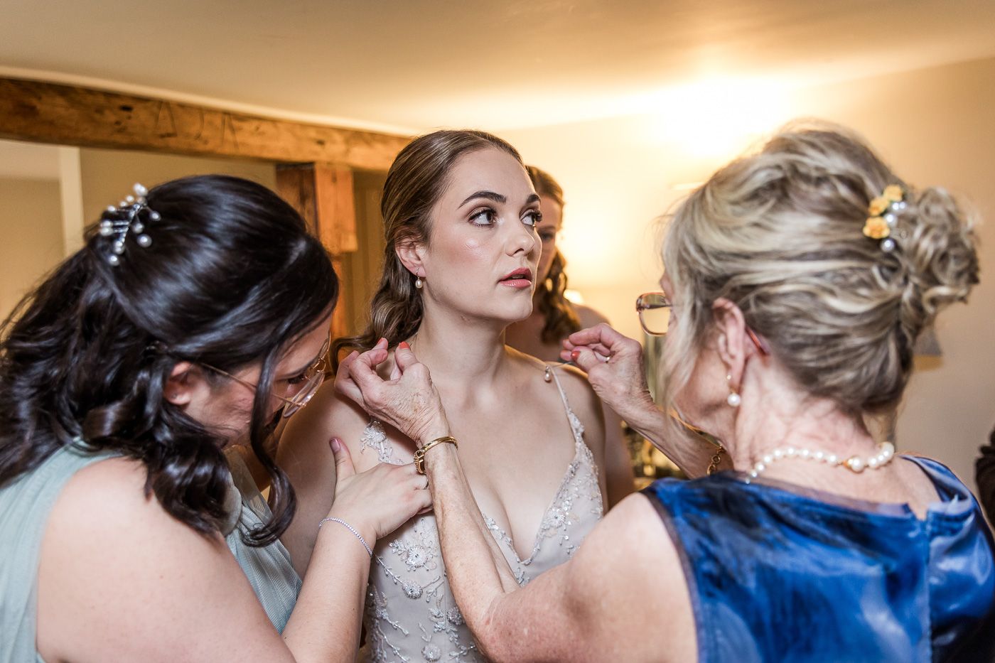 Bridesmaids in blue dresses help with wedding preparations indoors.