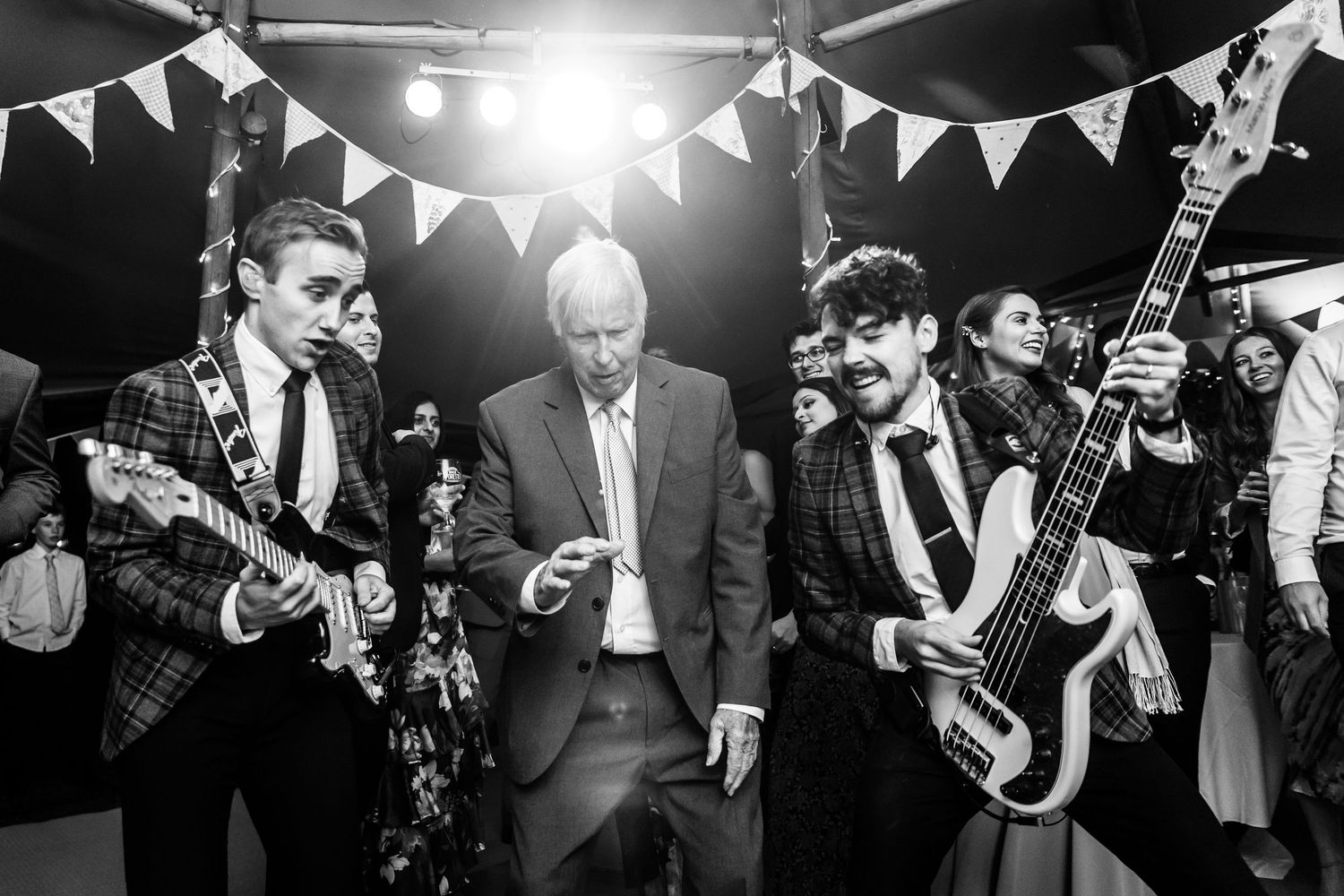 Black and white photo of a lively wedding reception with bunting decorations and musicians performing.