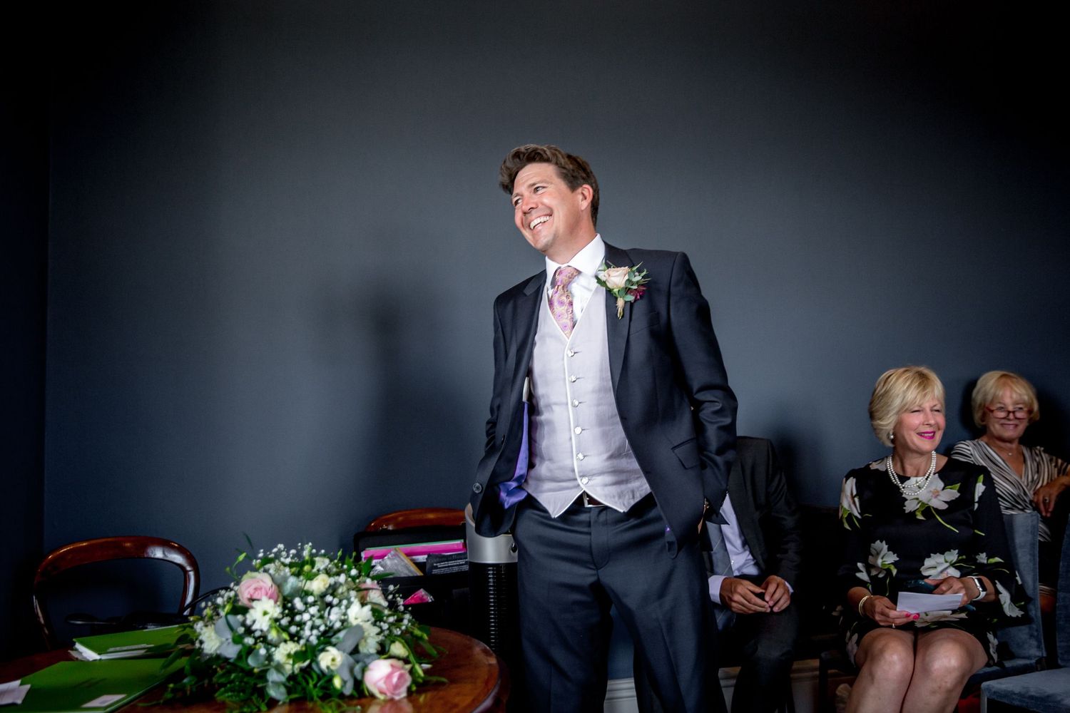 Wedding celebration candid moment in dark room with floral arrangements.