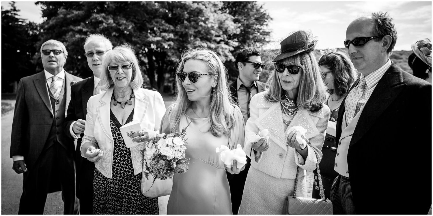 A group of wedding guests mingle and chat outdoors while holding drinks at an elegant garden reception.