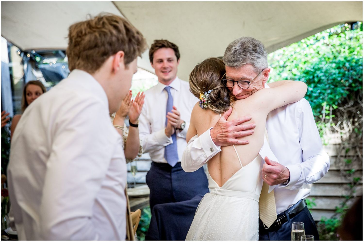 Casual outdoor wedding celebration with guests mingling at decorated tables under natural lighting.
