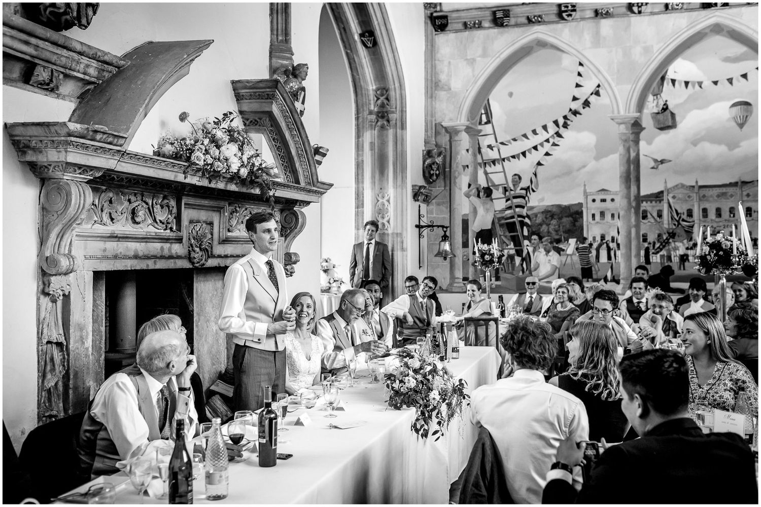 Wedding reception speech in a grand historic hall with arched ceilings and decorative bunting.