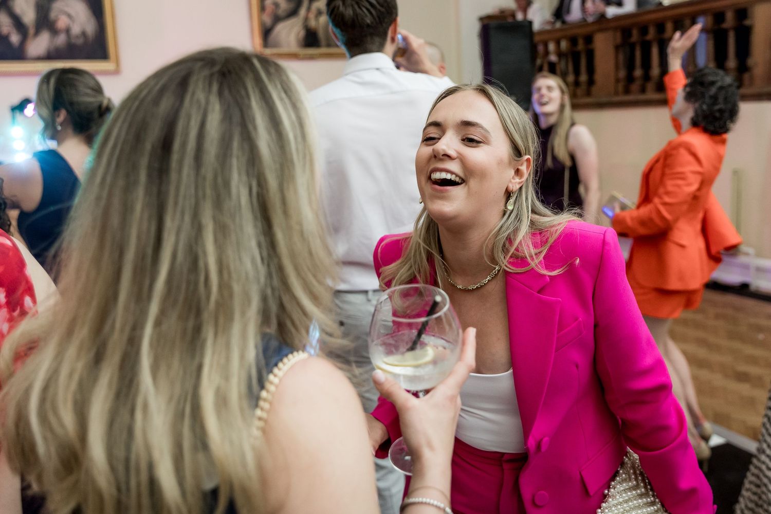 Guests dancing and laughing at a wedding reception with vibrant pink and orange outfits.