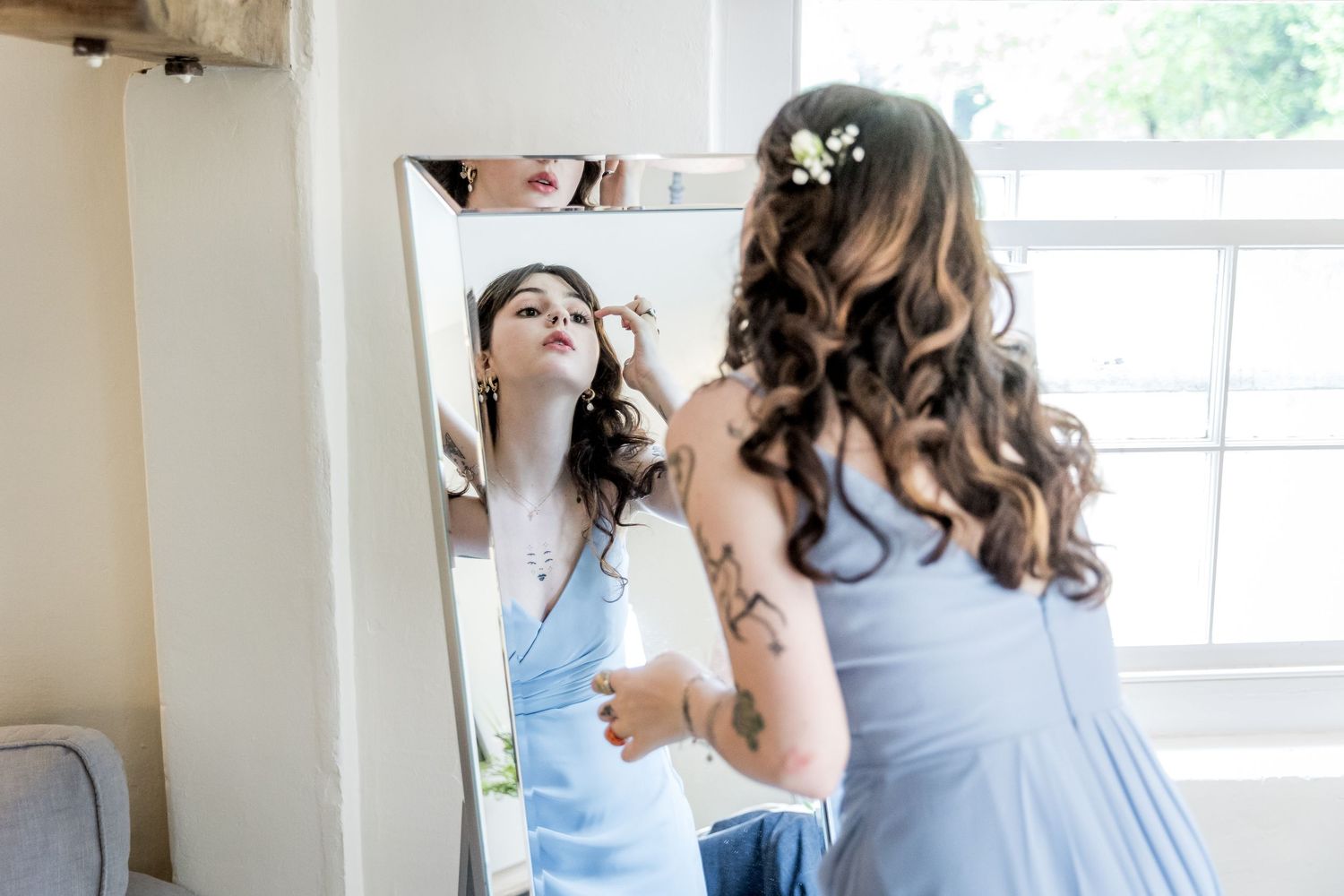Bridesmaids in pale blue dresses assist with wedding day preparations in a bright room.