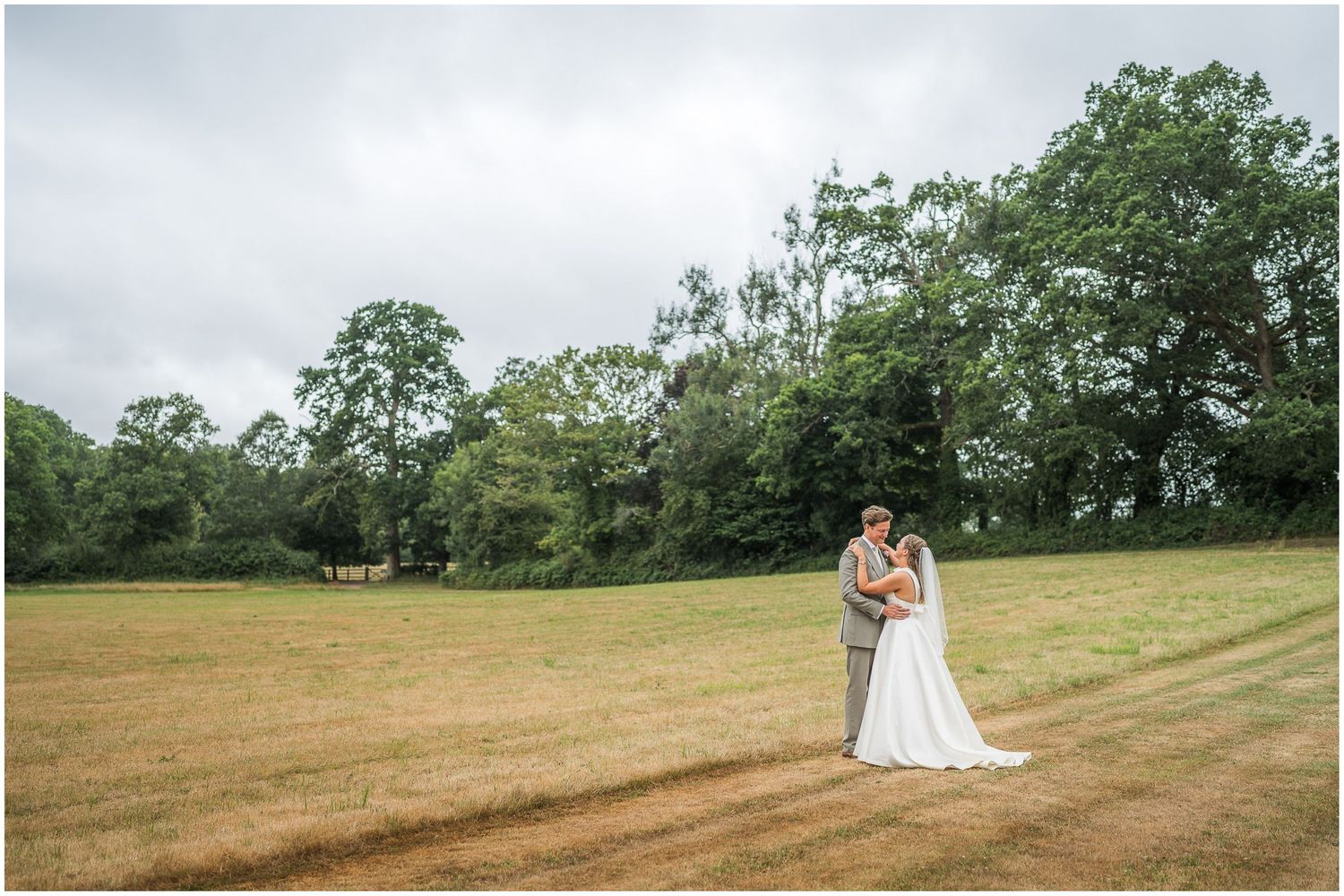 Couple portrait in the sunshine with bride and groom in the fields beyond the Holywell Estate's walled garden