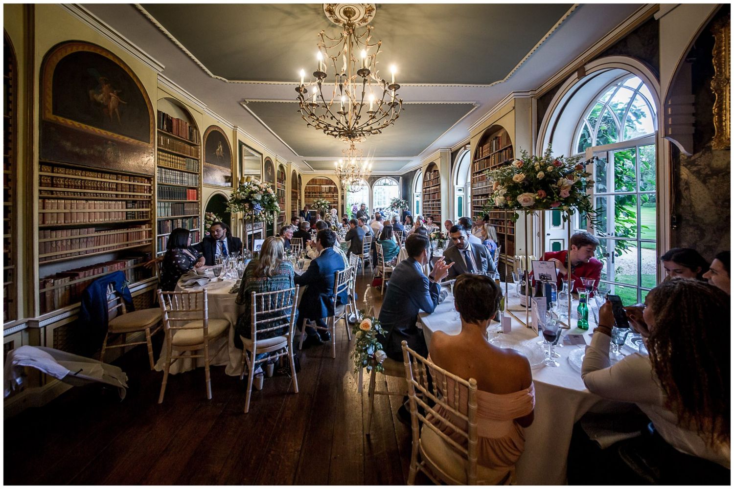 Panoramic view of an elegant wedding reception hall with crystal chandeliers and arched windows.