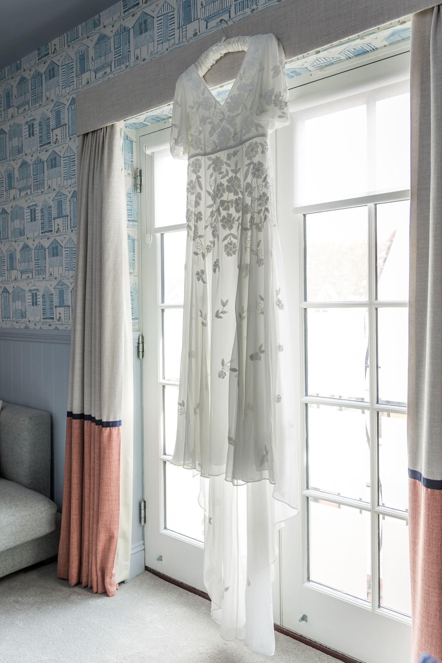 Light-filled room with blue wallpaper, white curtains, and pink color accents.
