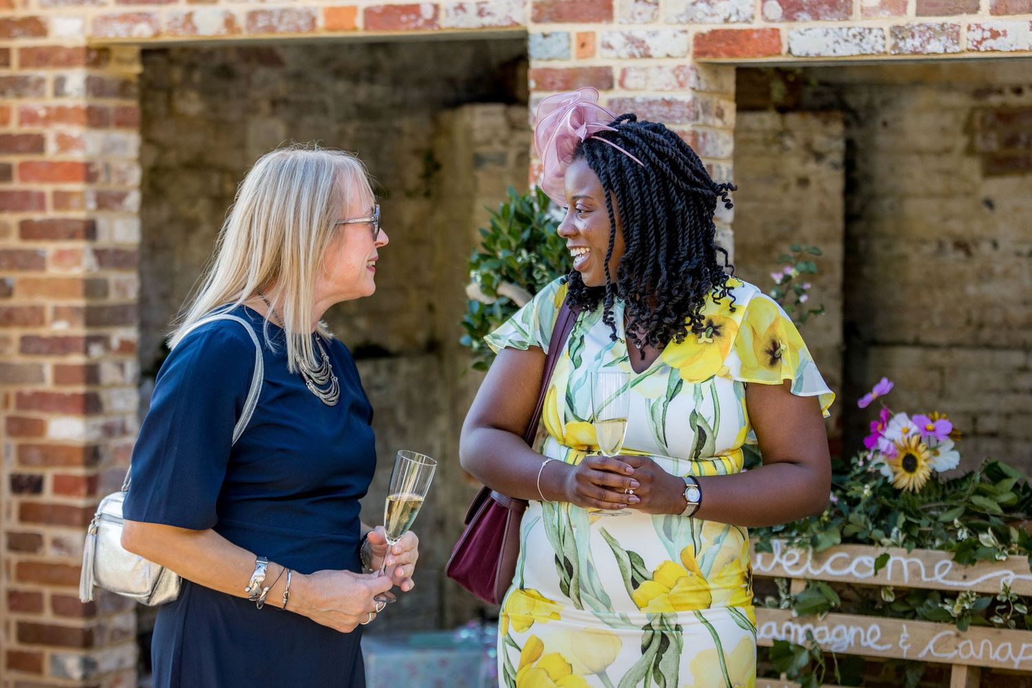 Guests in summer attire chat and mingle at a garden party near brick archways.