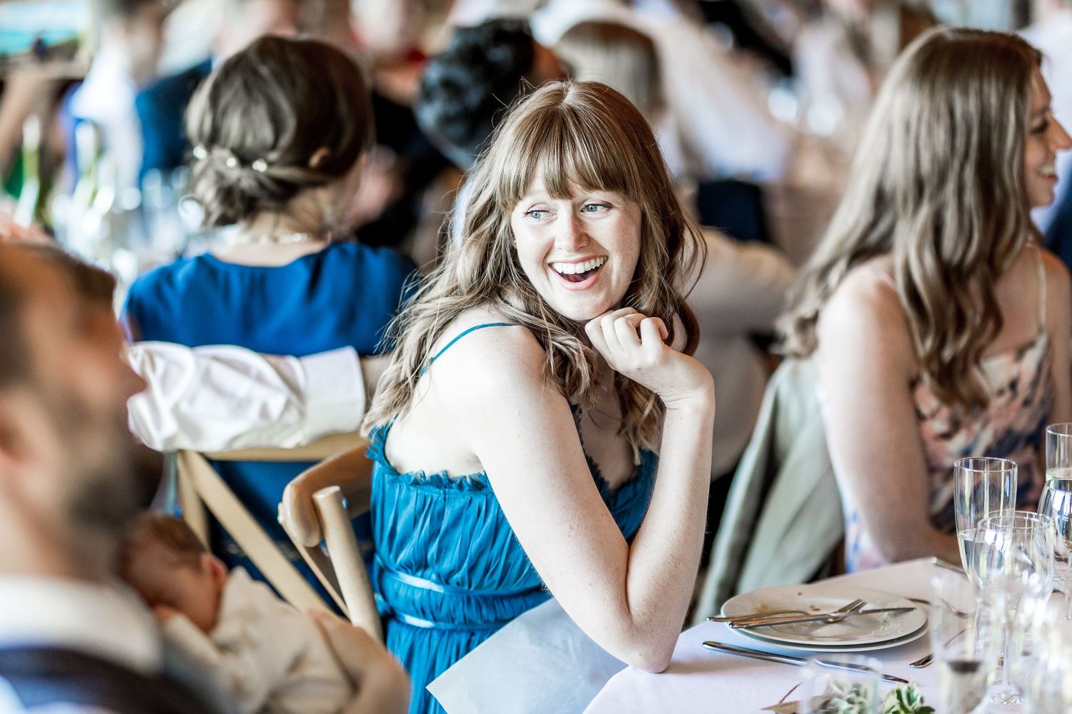 Wedding guests in blue attire smile and laugh during reception celebrations.