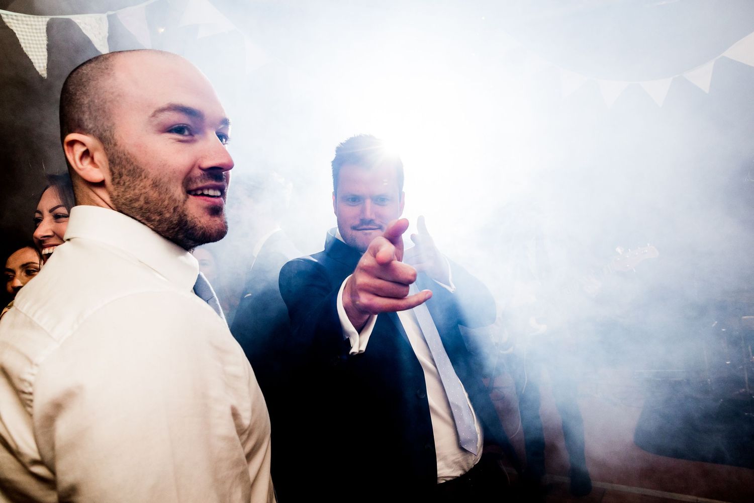 Party guests laugh and dance in atmospheric smoke at a wedding reception.
